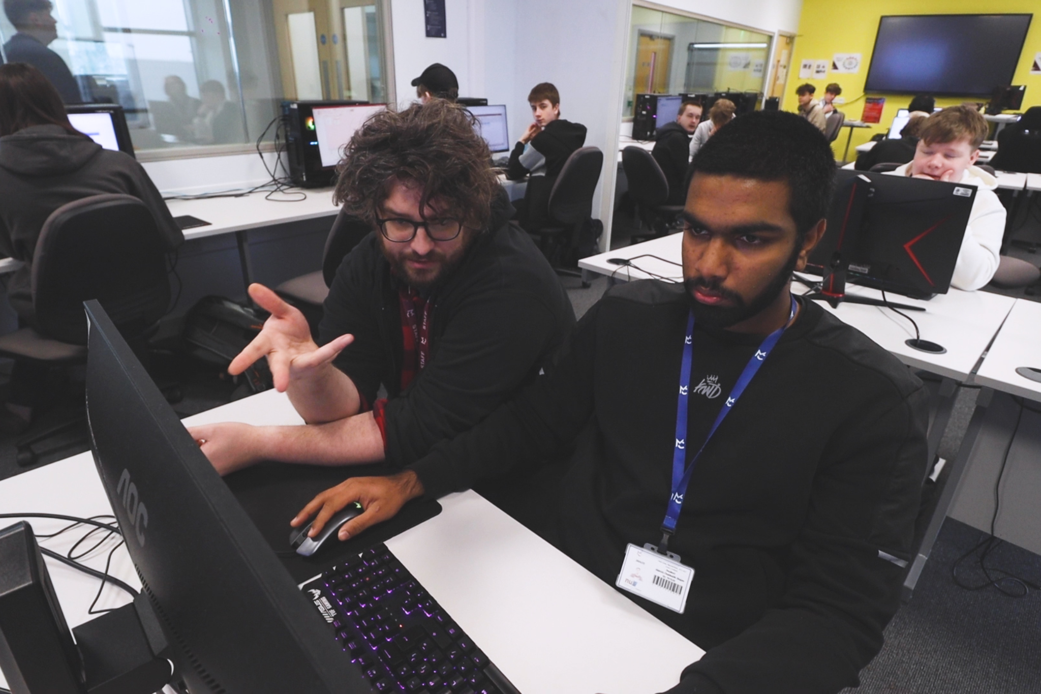 A Computing teacher is working with a student at the computer during class, offering guidance and support.