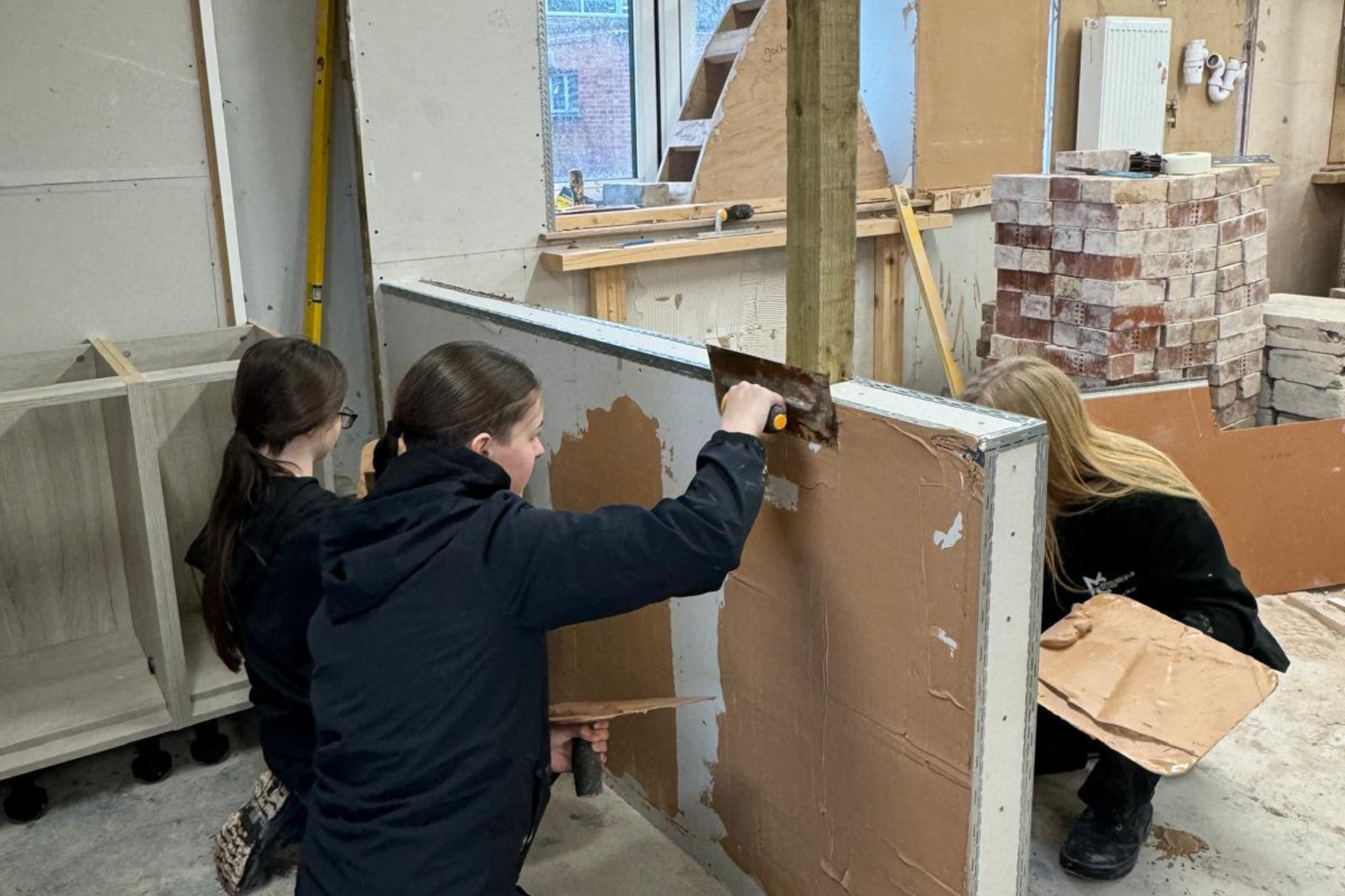 Two female construction students are plastering a wall