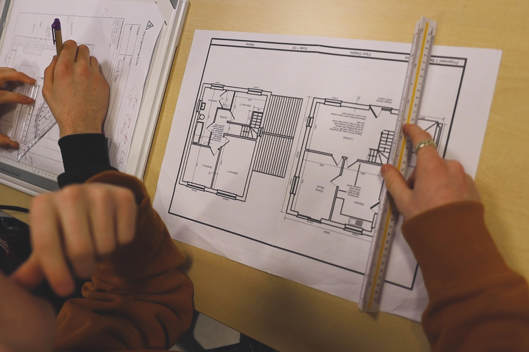 A student is using a ruler to measure a construction drawing plan.