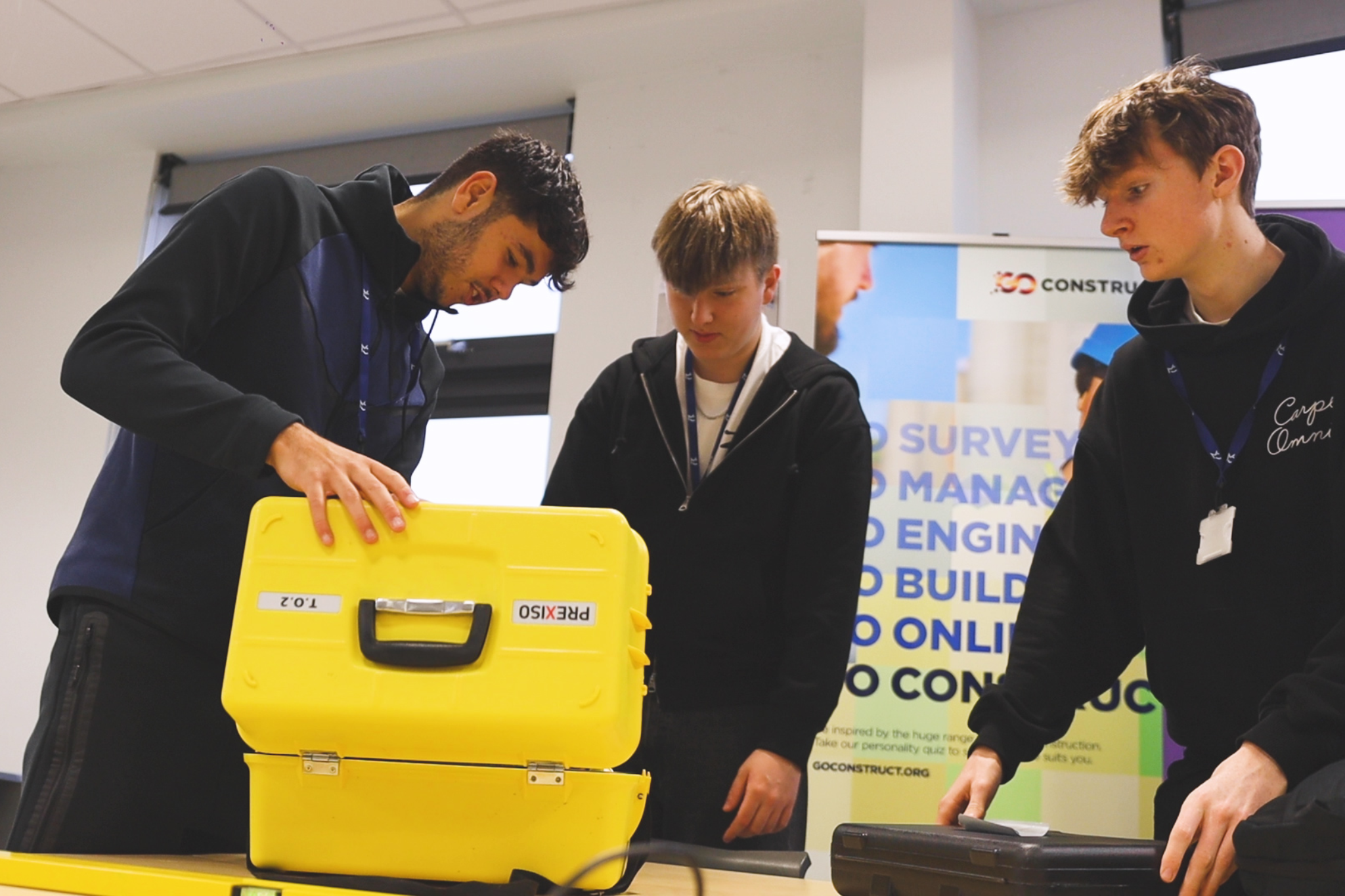 Three students are looking at surveying equipment