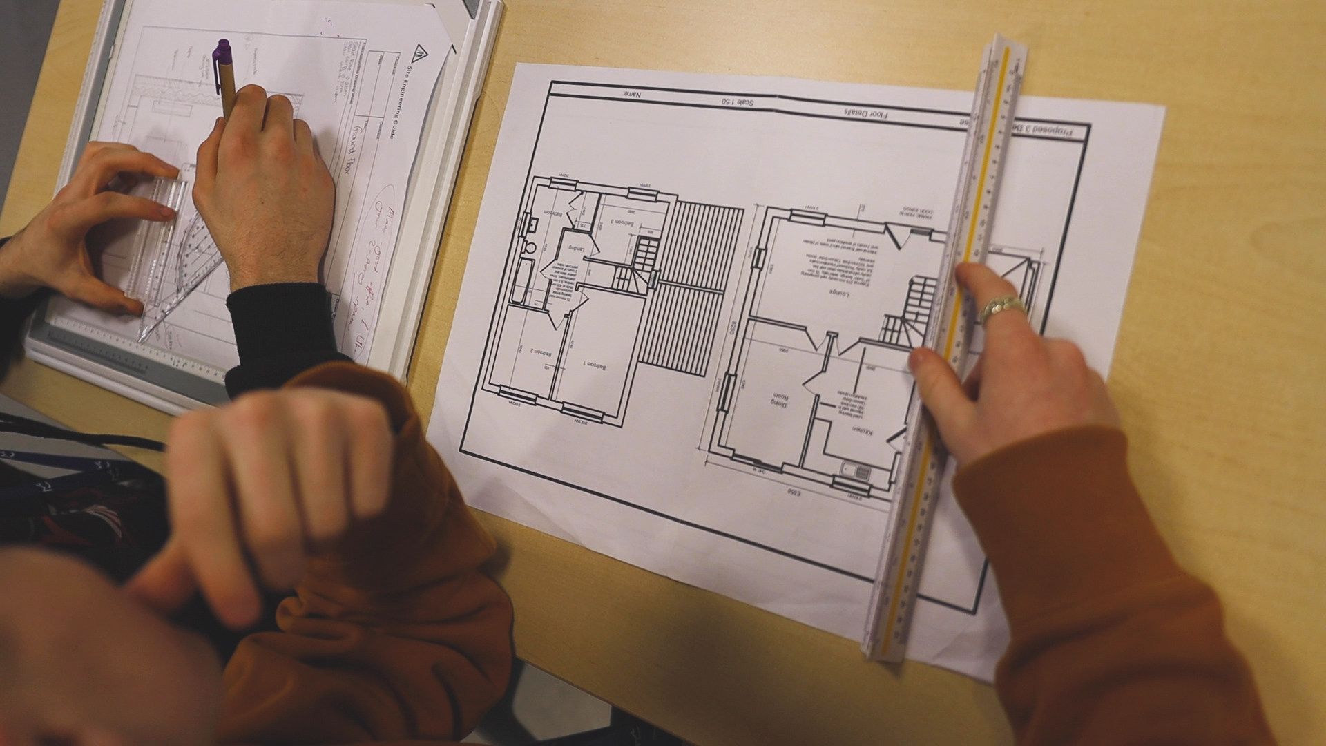 A student is using a ruler to measure a construction drawing plan.