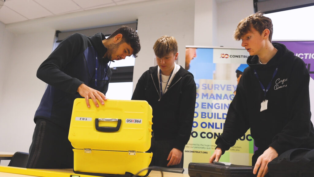 Three students are looking at surveying equipment