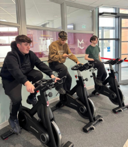 three students riding spin bikes