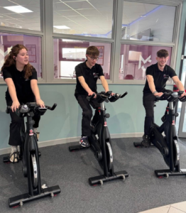 three students riding spin bikes