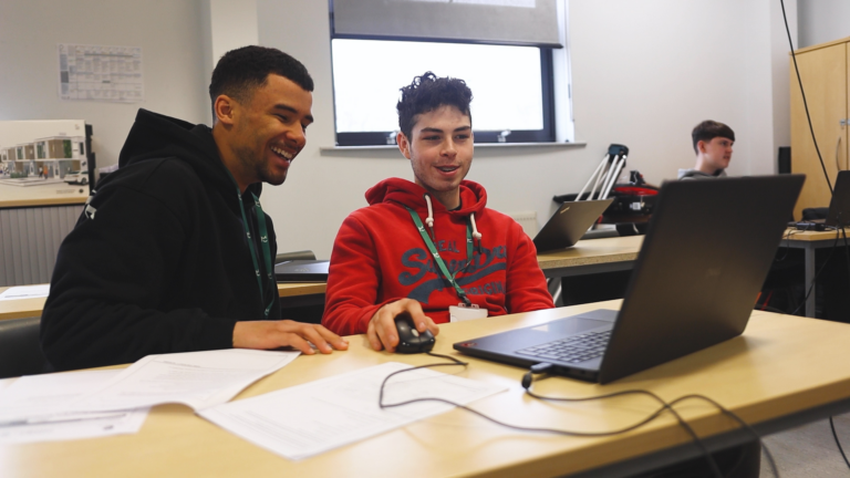 two students smiling whilst working on a computer