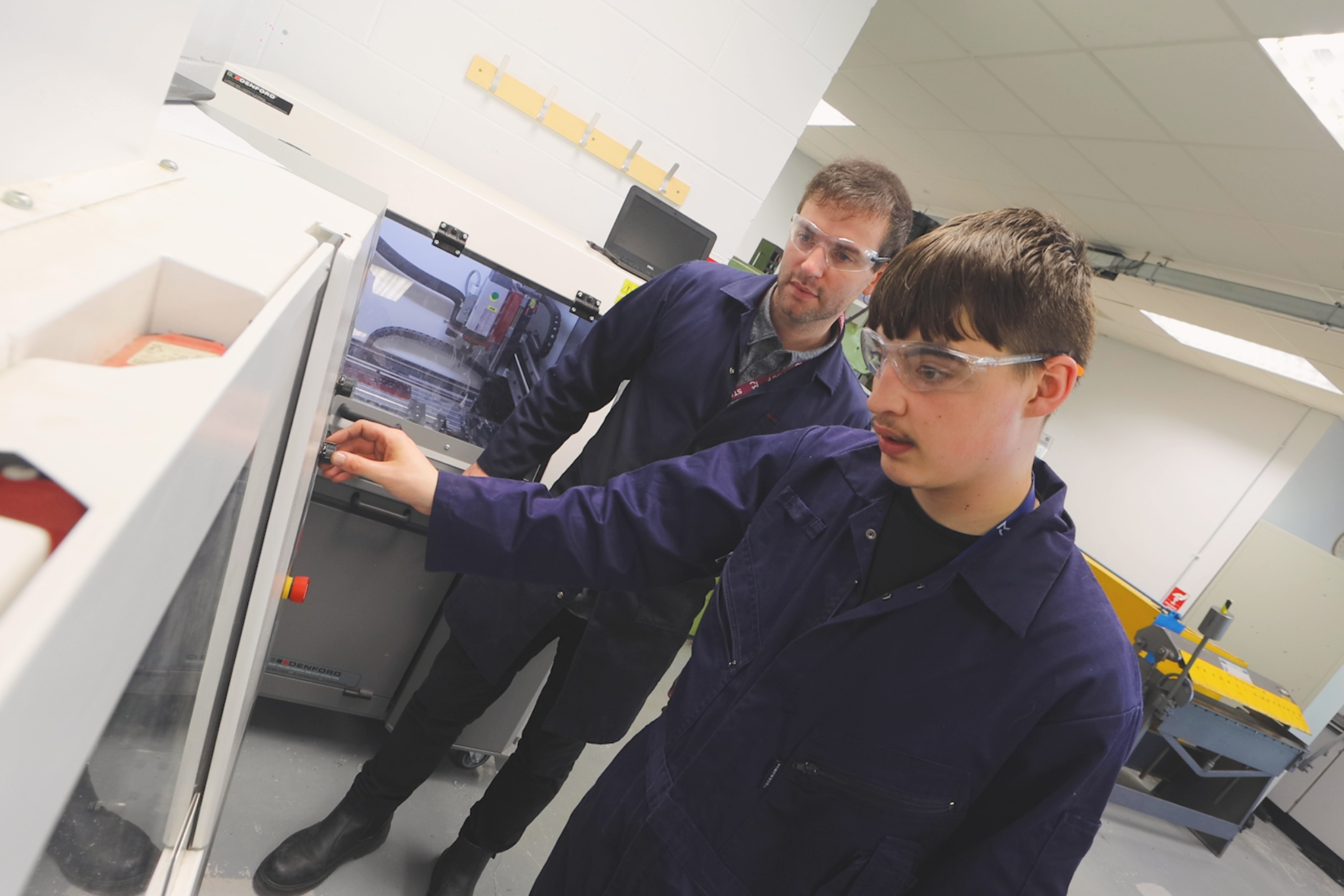 A teacher and an Engineering student is looking at engineering machinery.