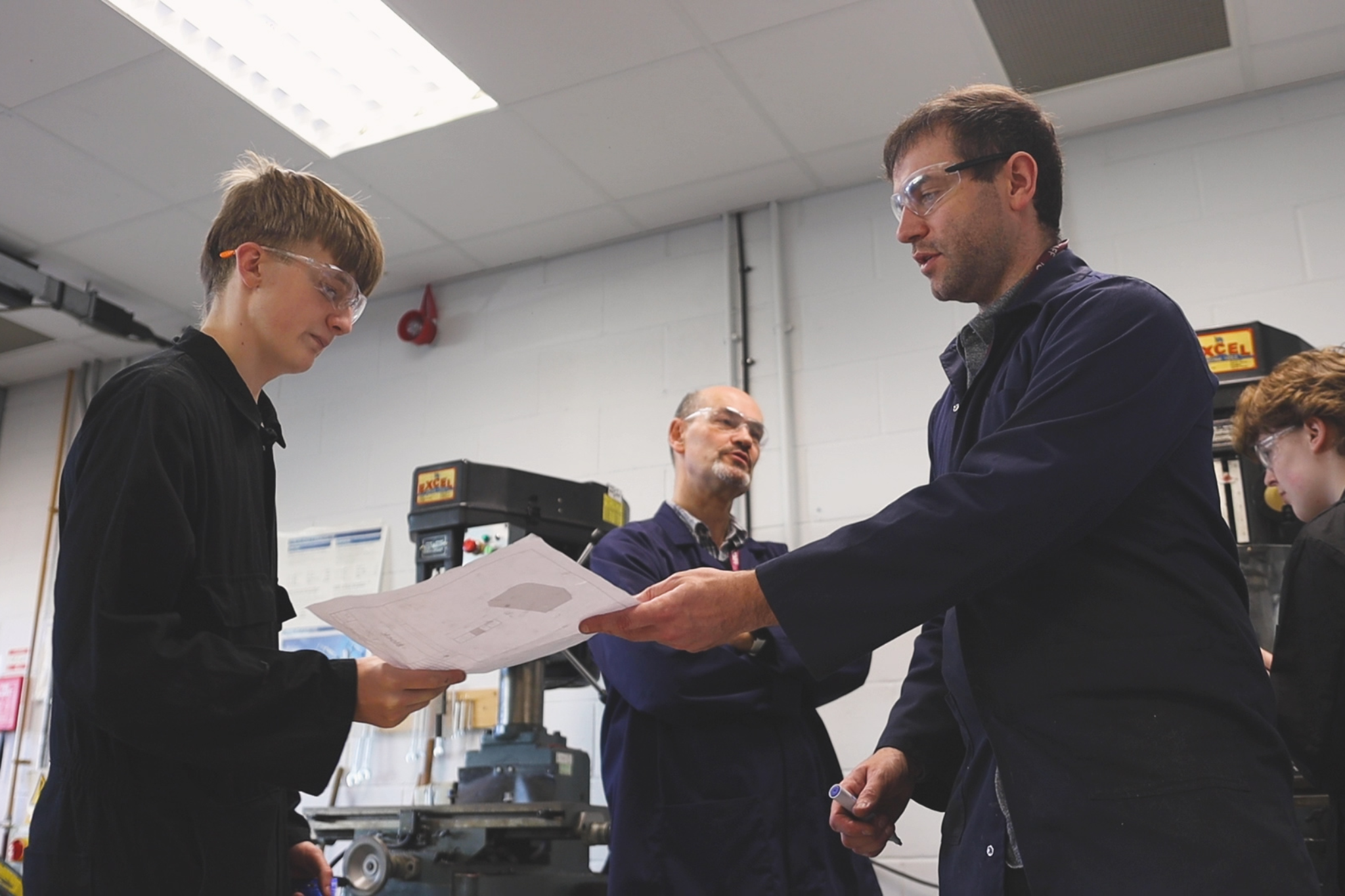 An Engineering teacher is handing a piece of paper to a student.