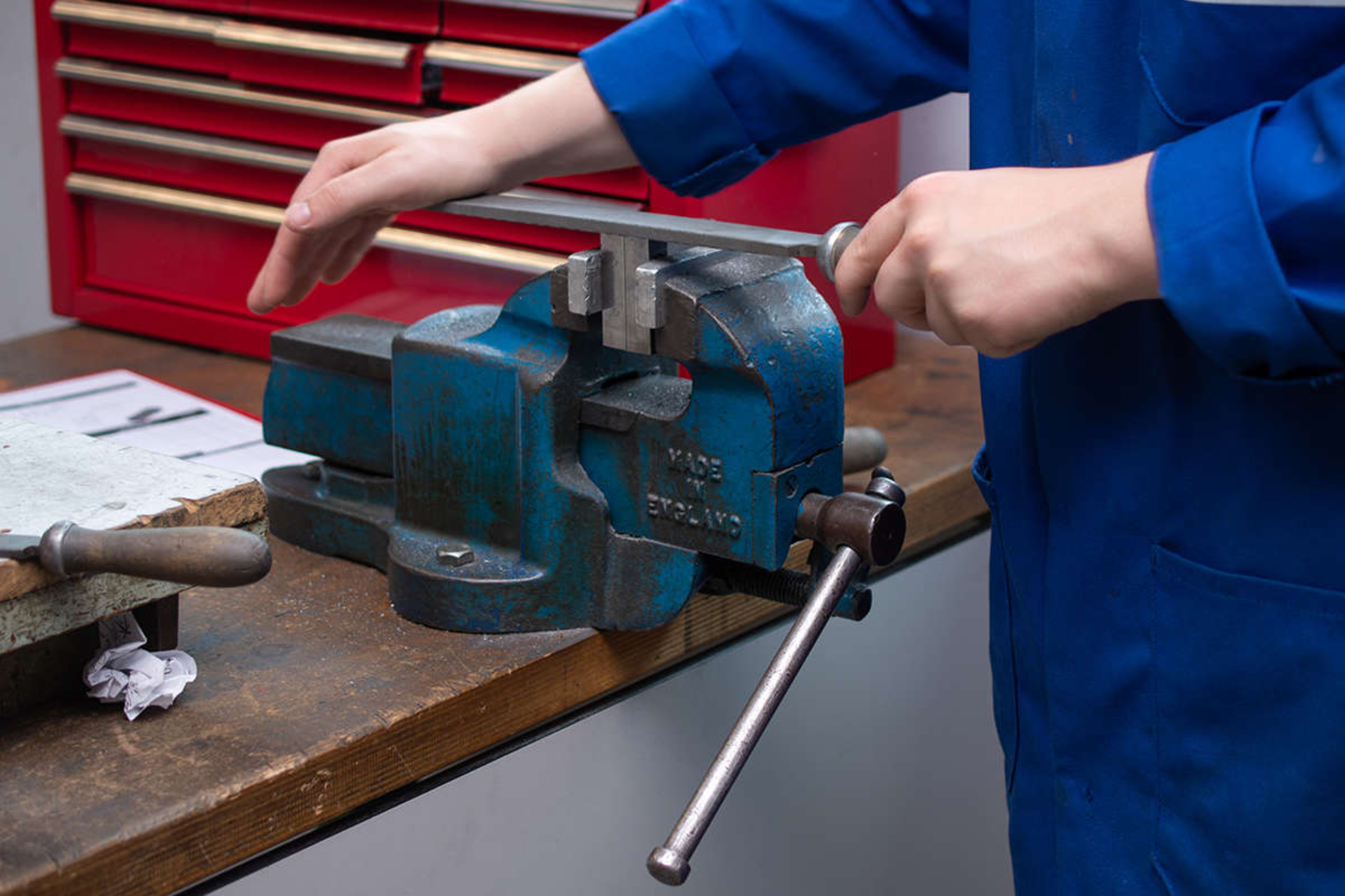 An engineering student is filing a piece of metal that is in a vice.