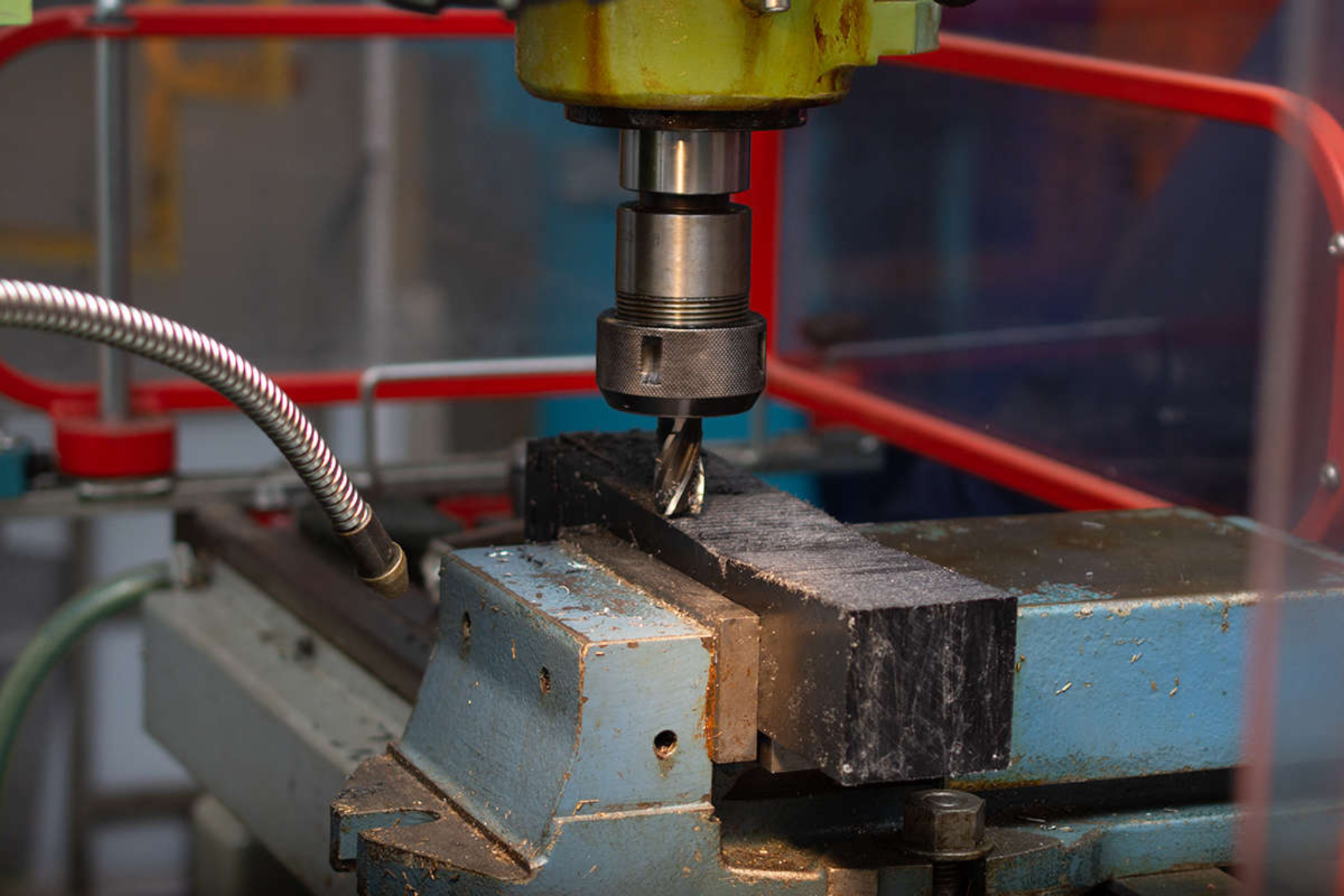 The image is a close up shot of engineering machinery, focusing on an object in a vice with a drill above it.