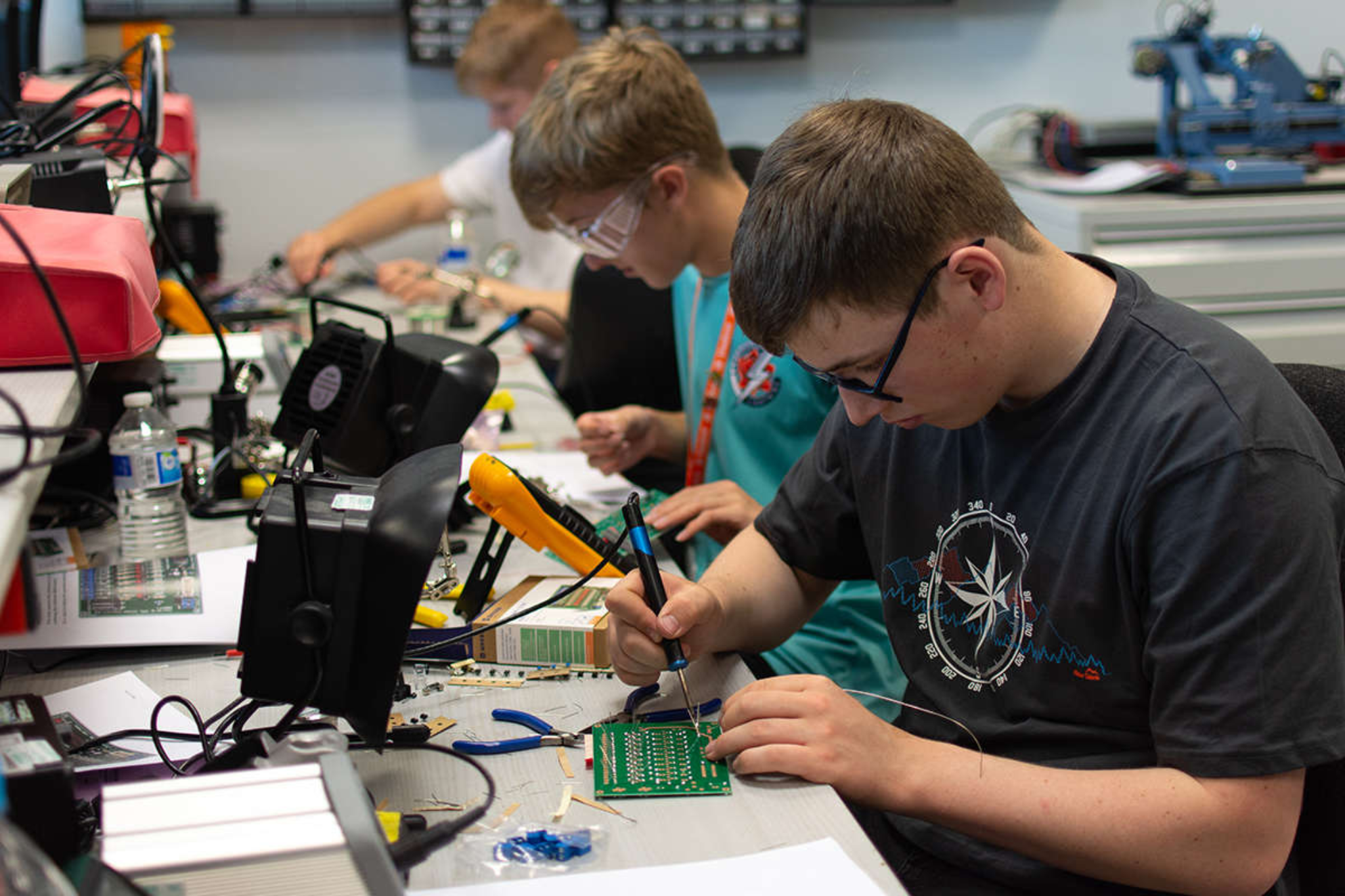 Three engineering students are soldering circuit boards