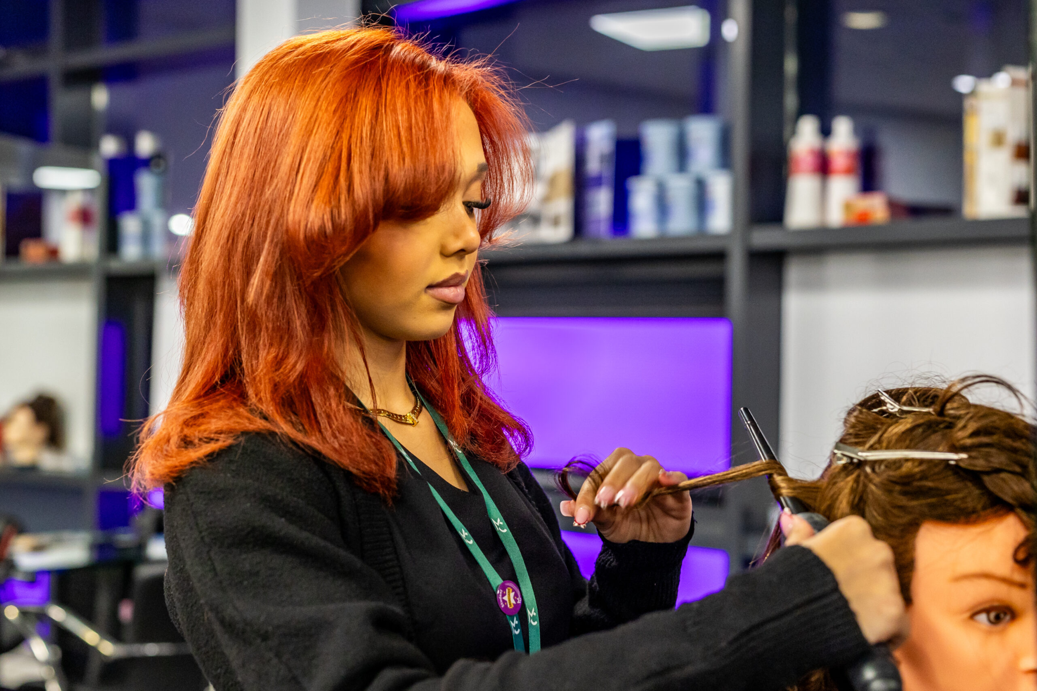 A hairdressing student is practising curling hair on a mannequin head