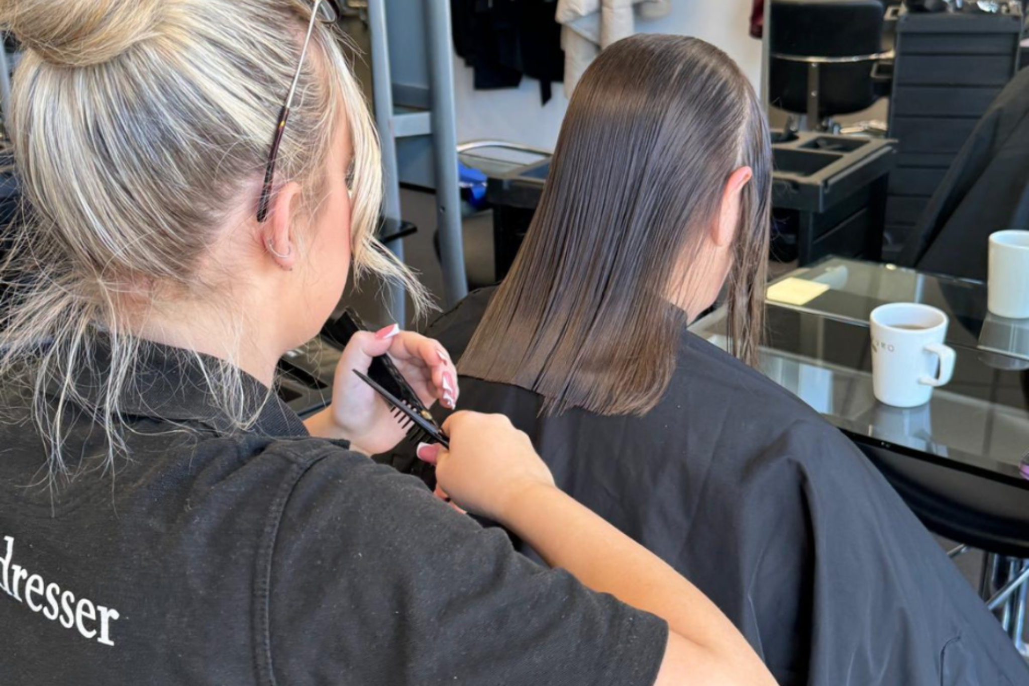 A Hairdressing apprentice is cutting a client's hair.