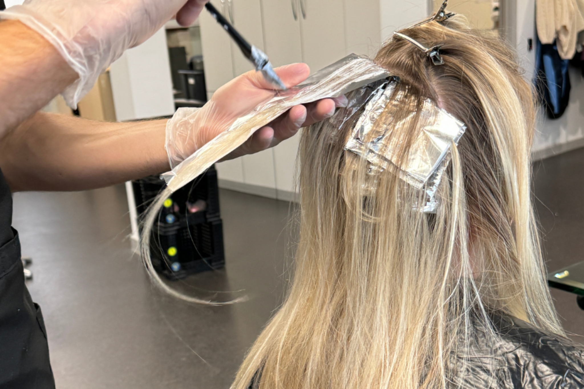 A hairdressing student is adding highlights to a client's hair.