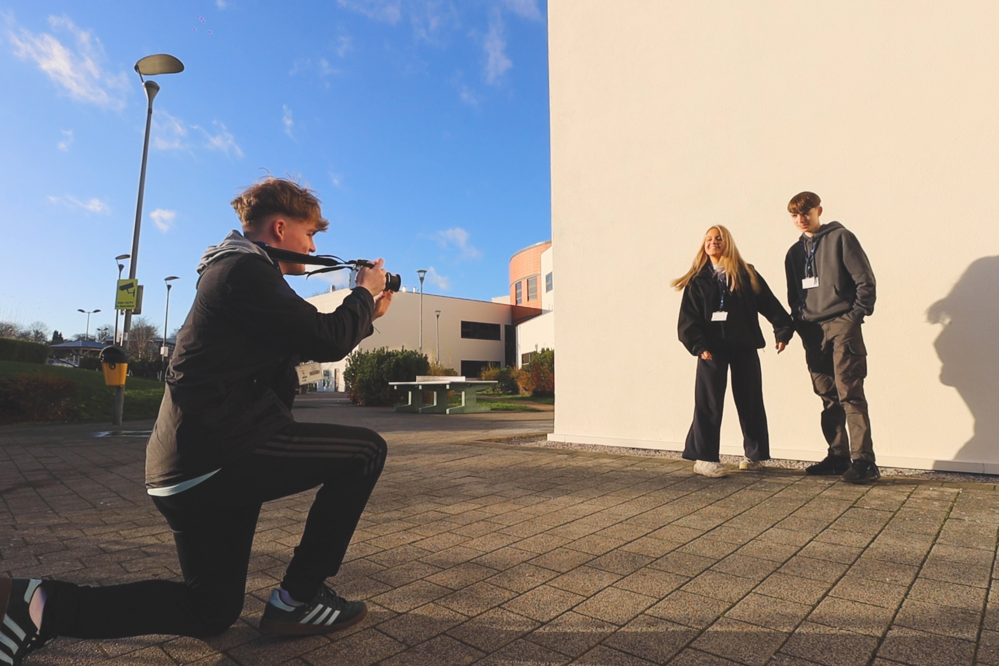 A Creative media student is taking a photo of two other students.