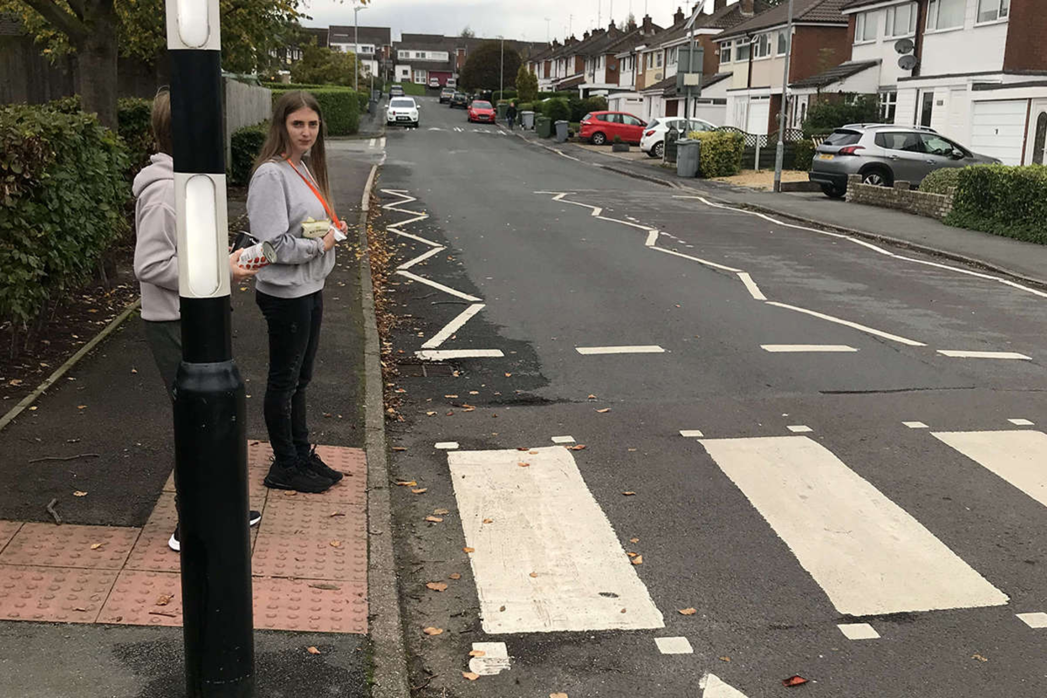 Two students stand at zebra crossing, waiting to cross