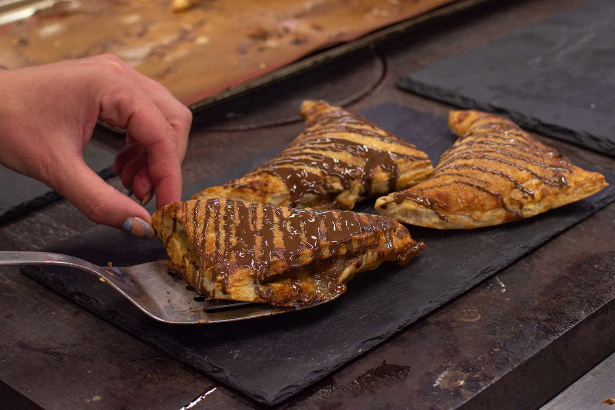 A hand is placing three chocolate pastries onto a black slate plate