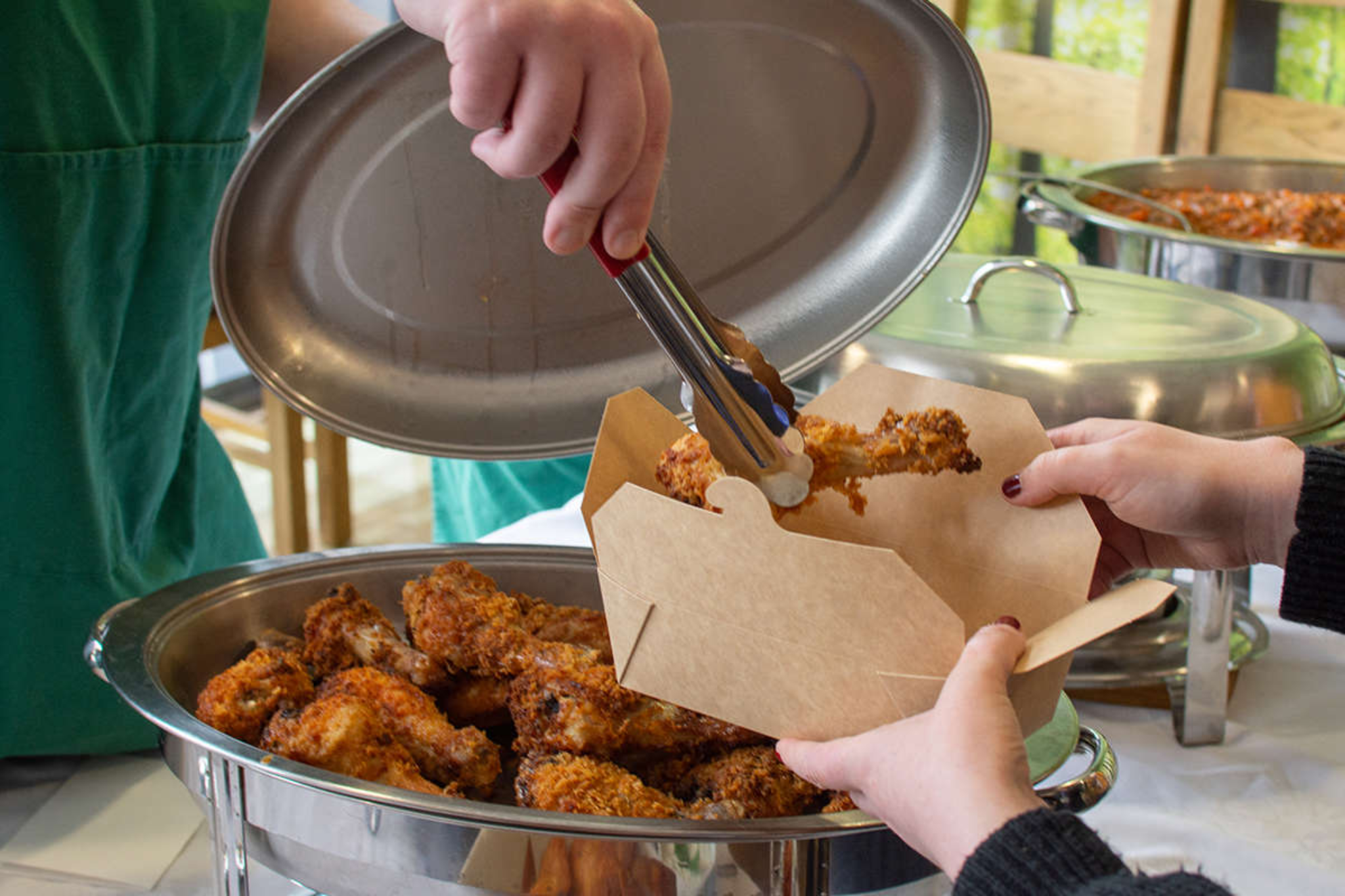 A student is placing a chicken drumstick into a cardboard takeaway box.