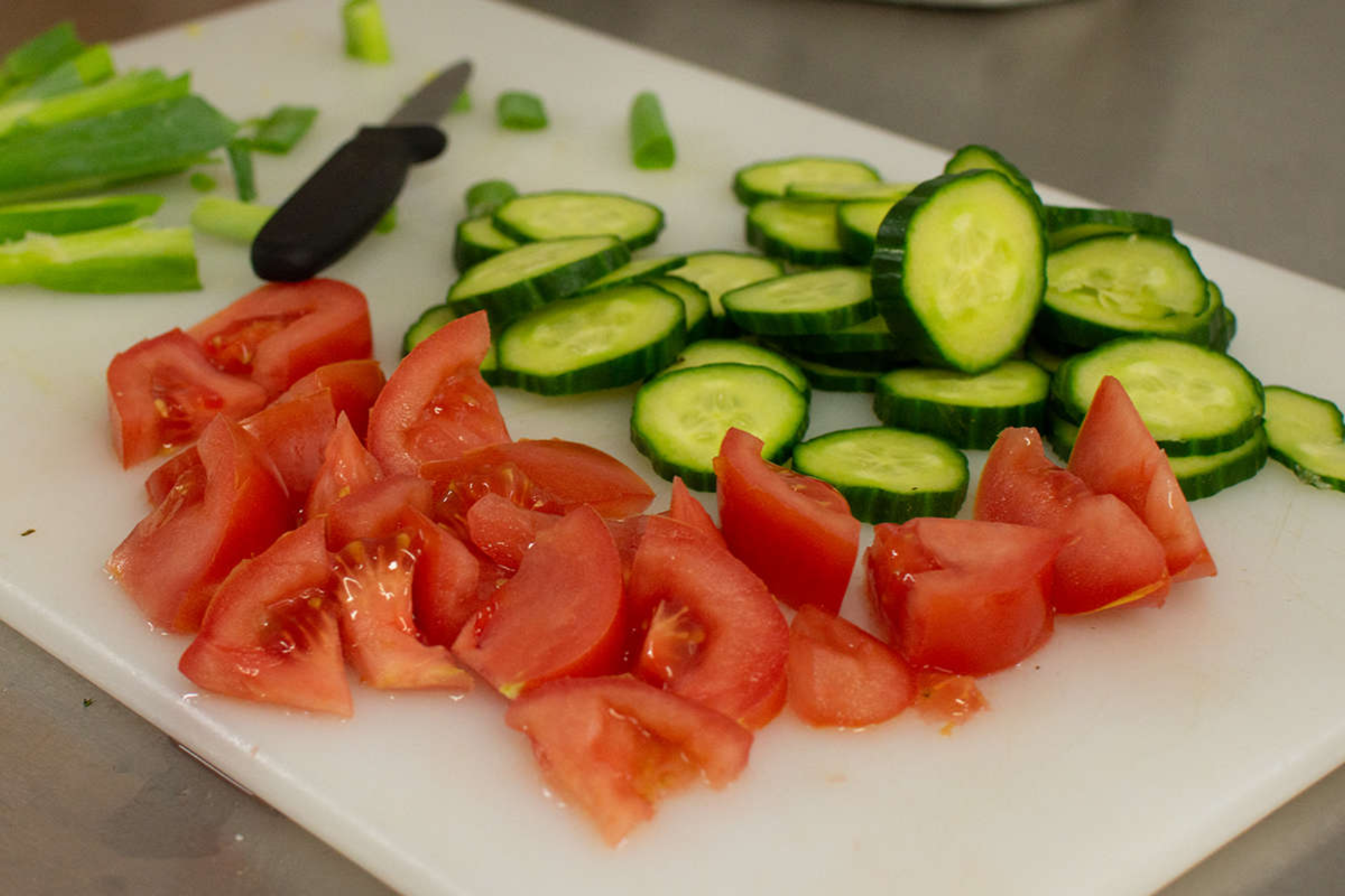 A white chopping board has freshly cut tomatoes and cucumbers placed on it