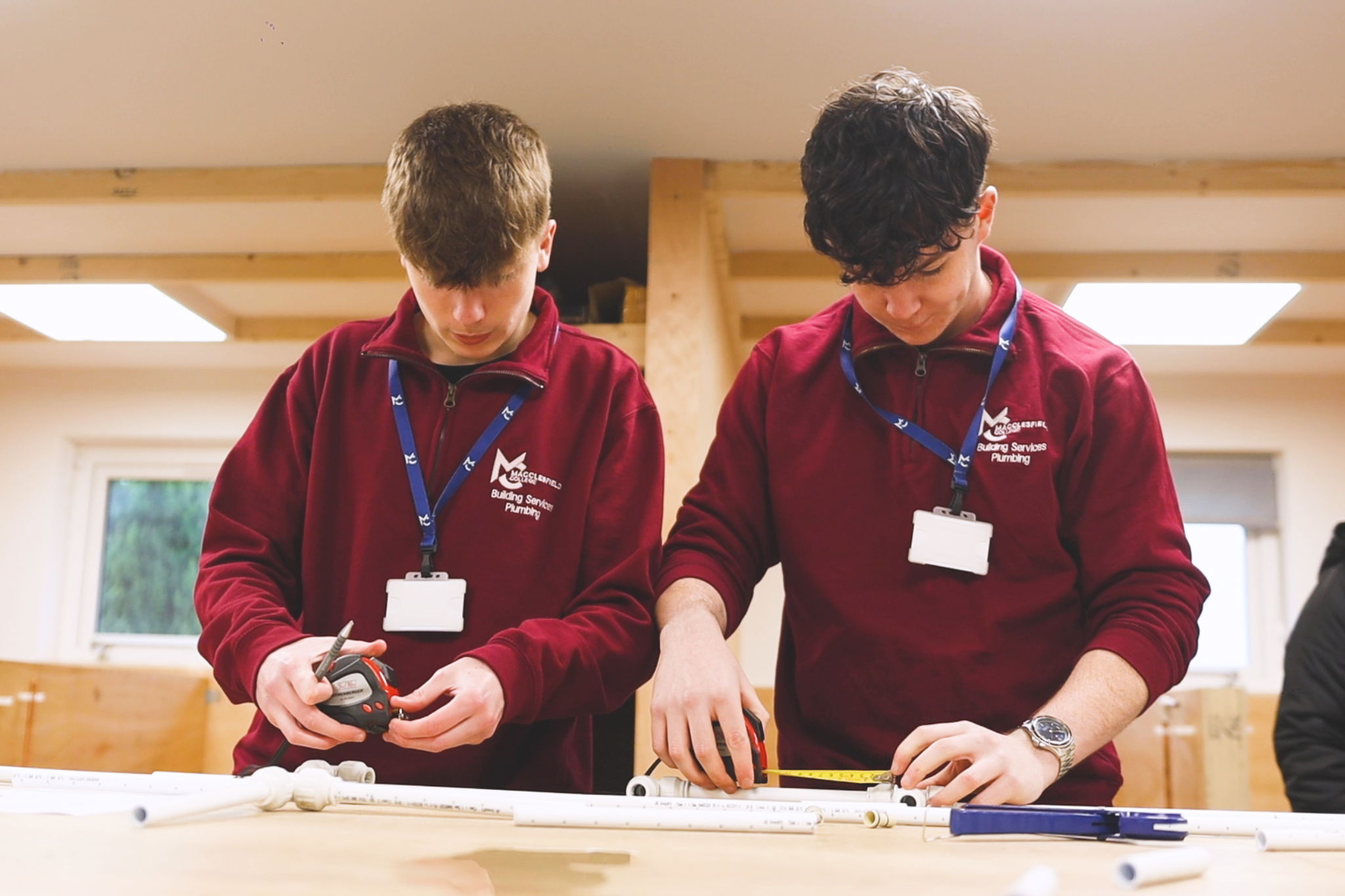 Two plumbing students measuring plastic pipes.
