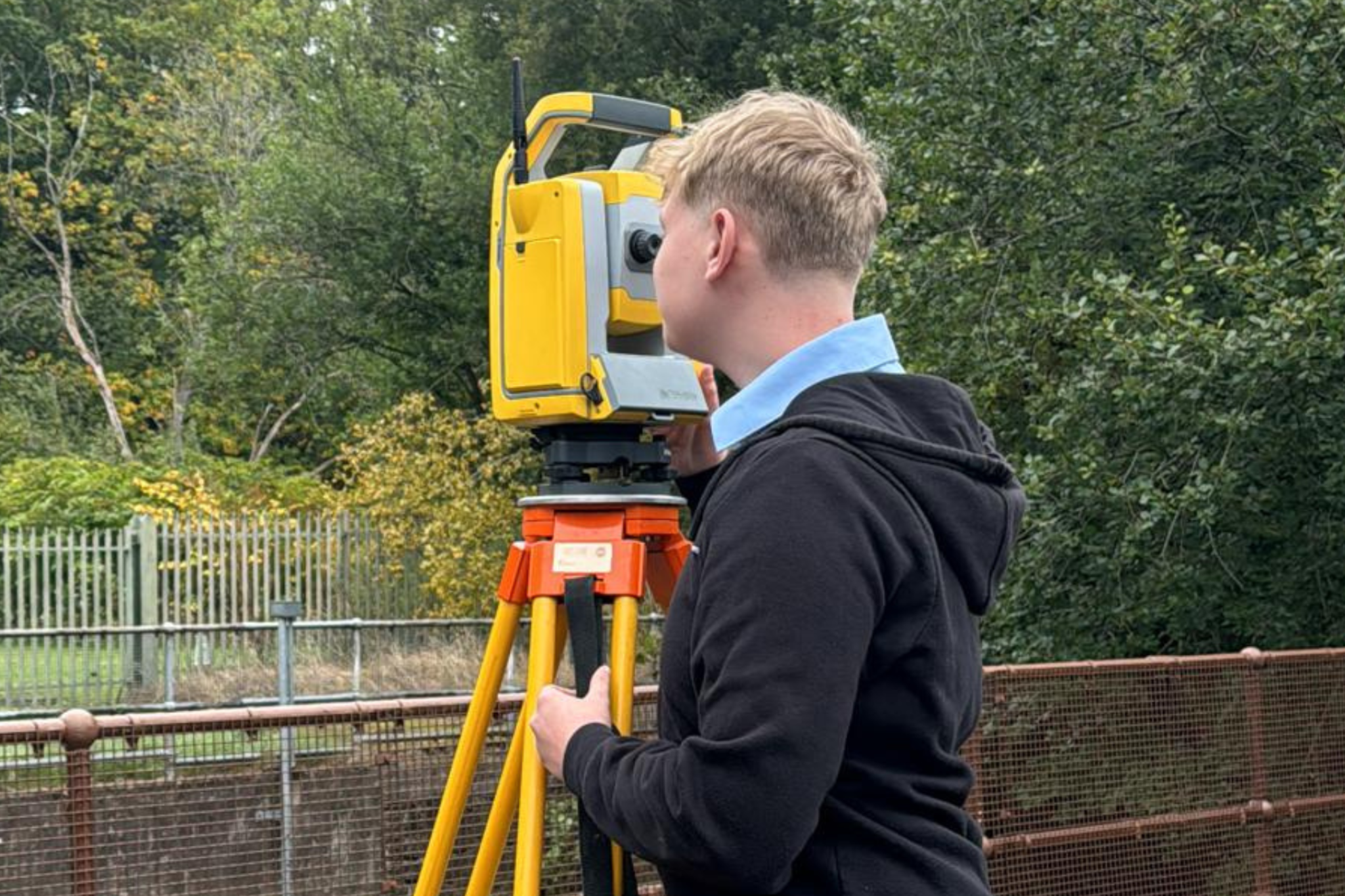A student is using surveying equipment on site.