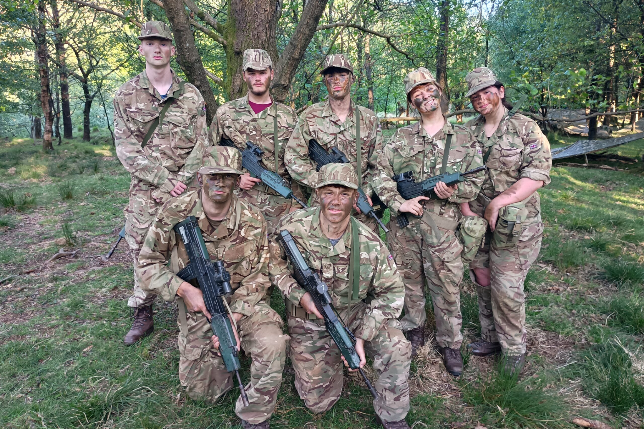 Public Service students are dressed in Army uniforms with their faces covered in camouflage paint, smiling for a photo.