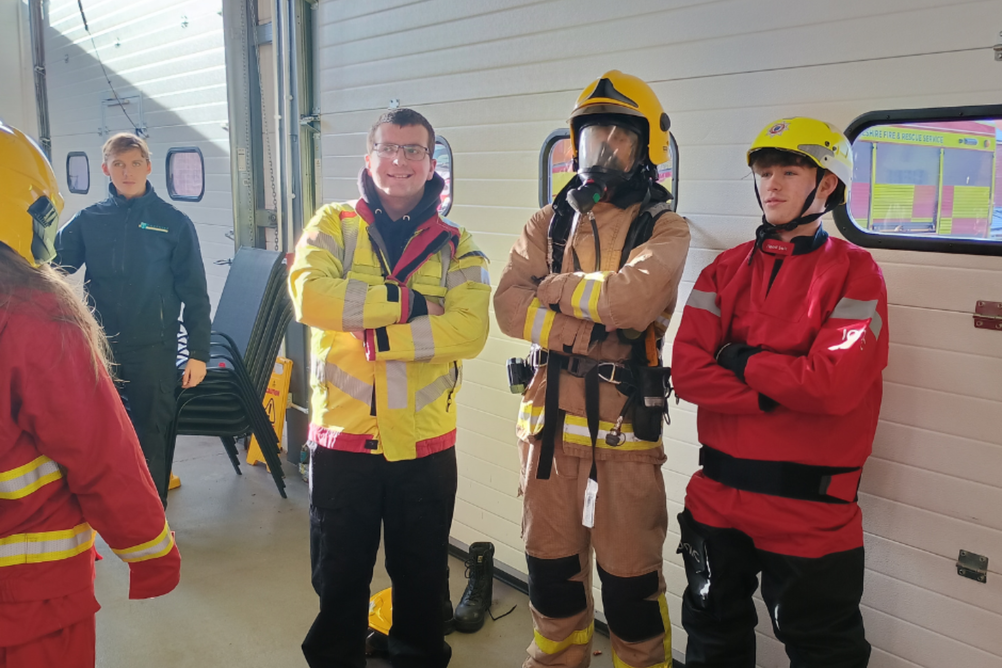 A group of Public service students are smiling wearing firemen uniforms, during their fire station trip.