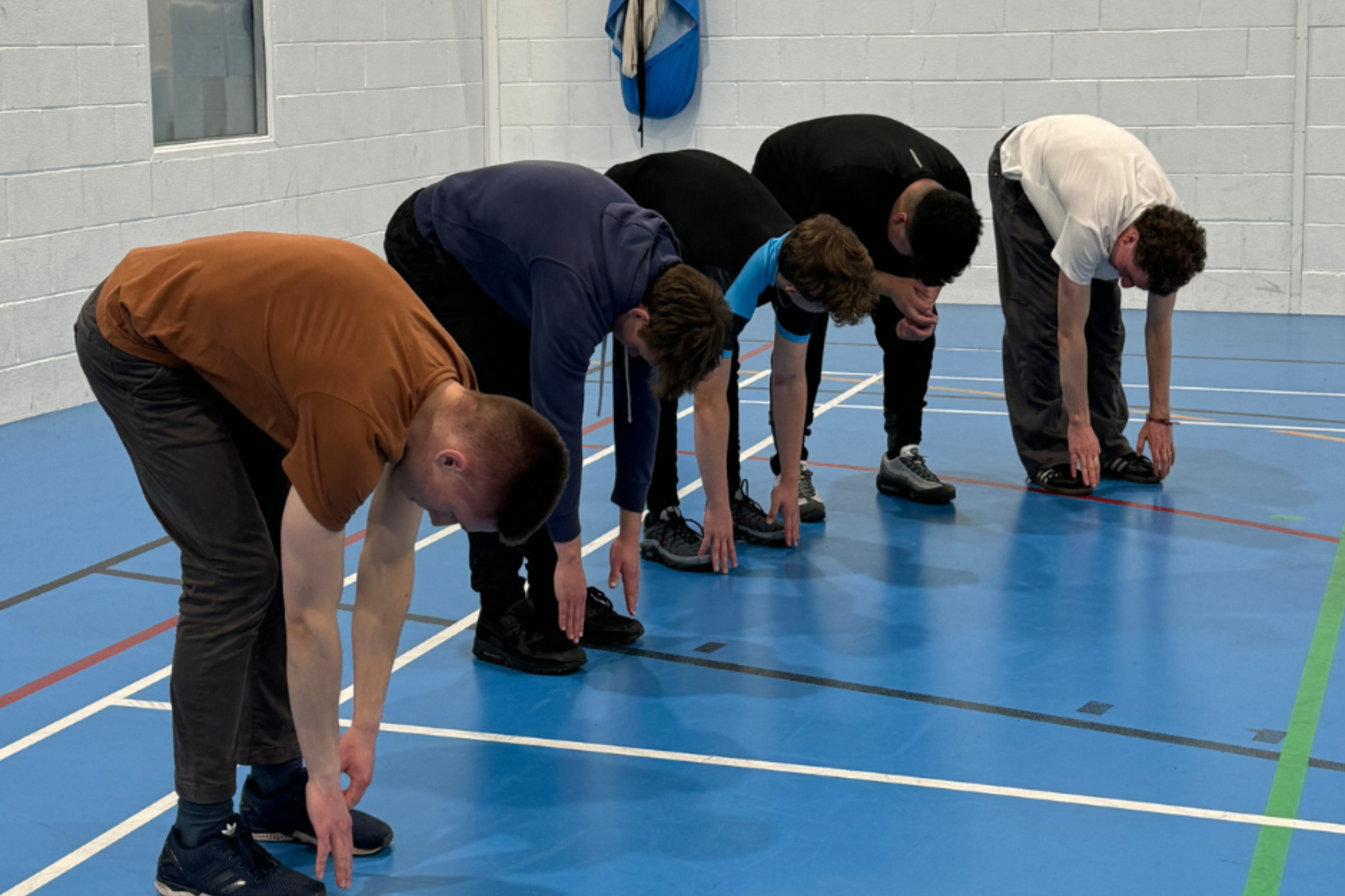 A group of sport students are practicing fitness techniques, bending down to touch their toes as part of their stretching routine.