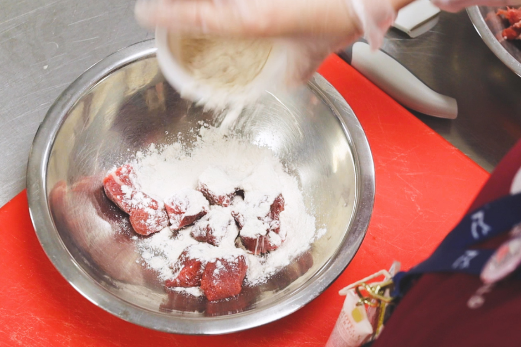 A Whites Chef Academy student is sprinkling flour over a bowl of meat.