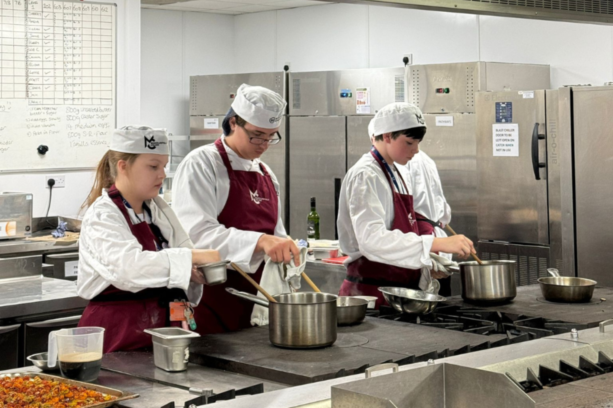 A group of Whites Chef Academy students are working in the kitchen, stirring pans.