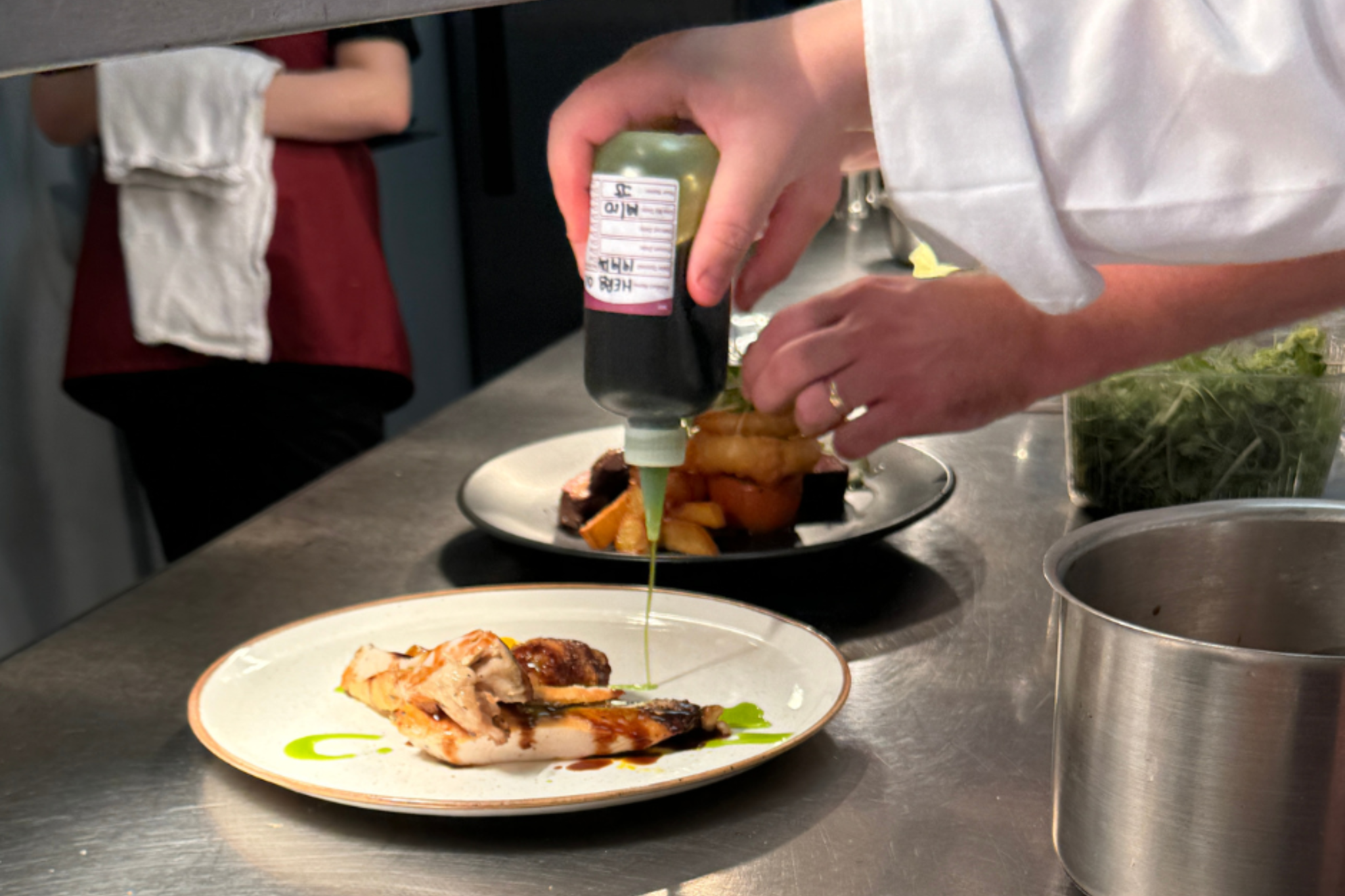 A Whites Chef Academy student is pouring a green sauce over a chicken dish.