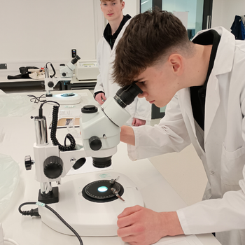 a student wearing a lab coat is looking into a microscope