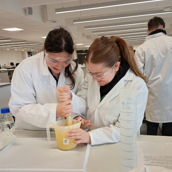 two students wearing lab coats are stirring custard in a jug