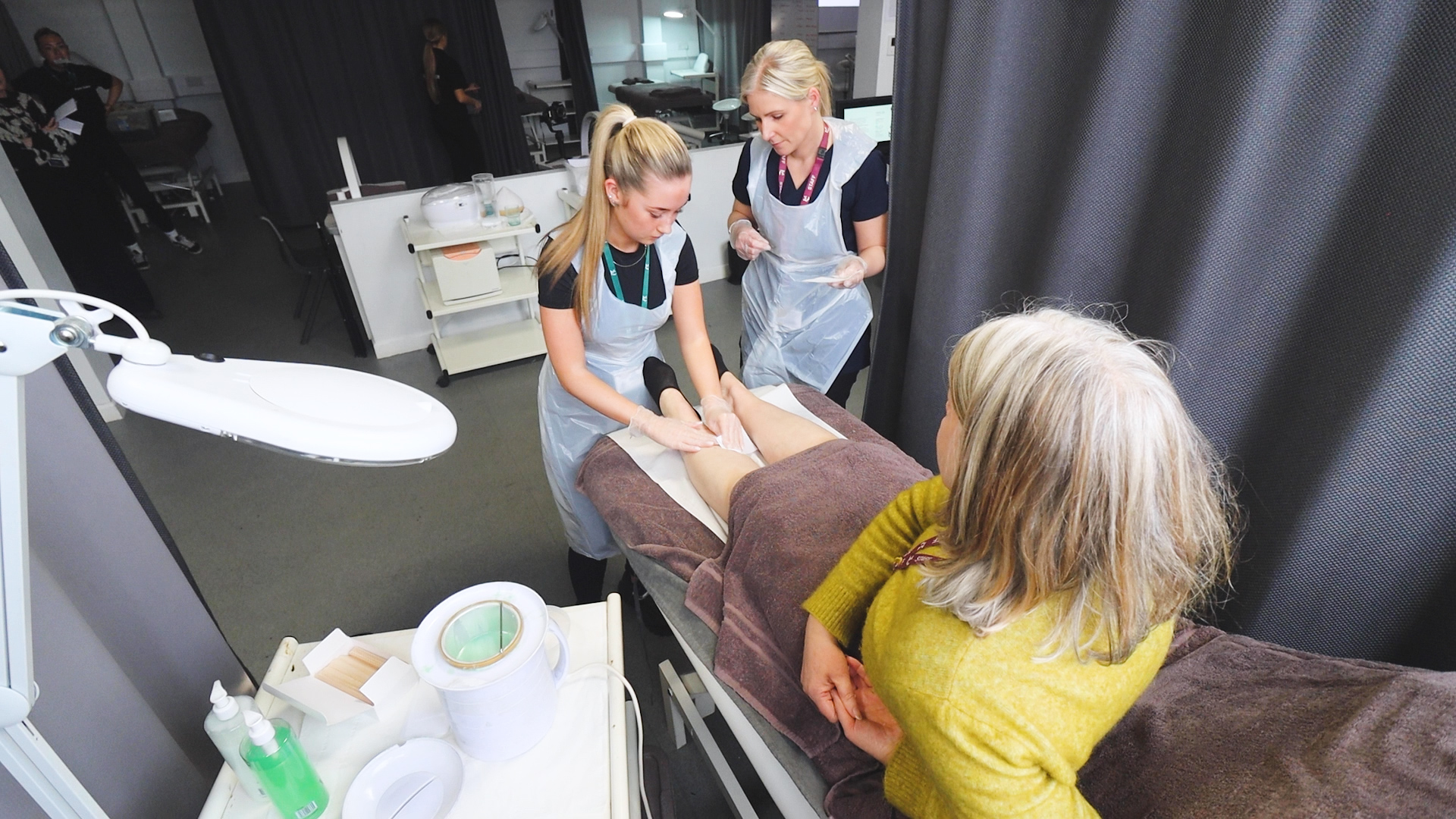 a beauty teacher observes a student completing a waxing treatment on a client