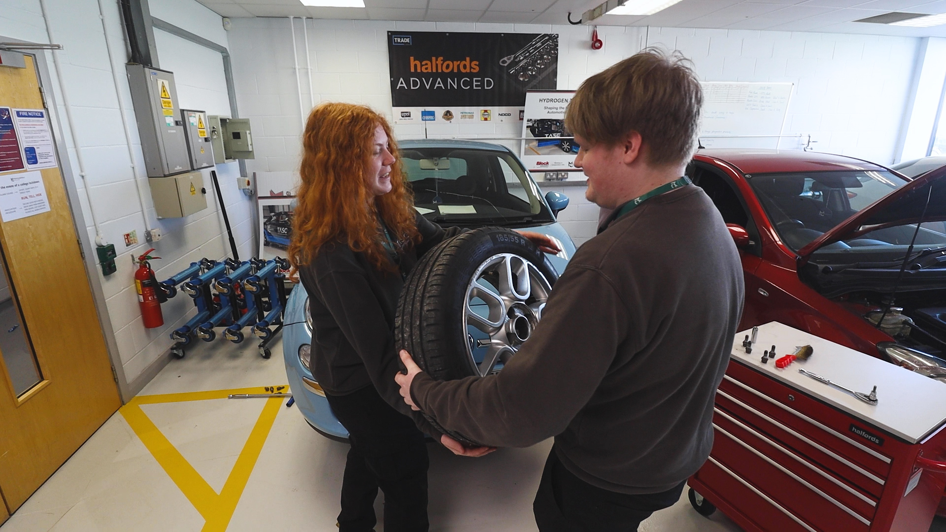 Two automotive students passing a car tyre to each other