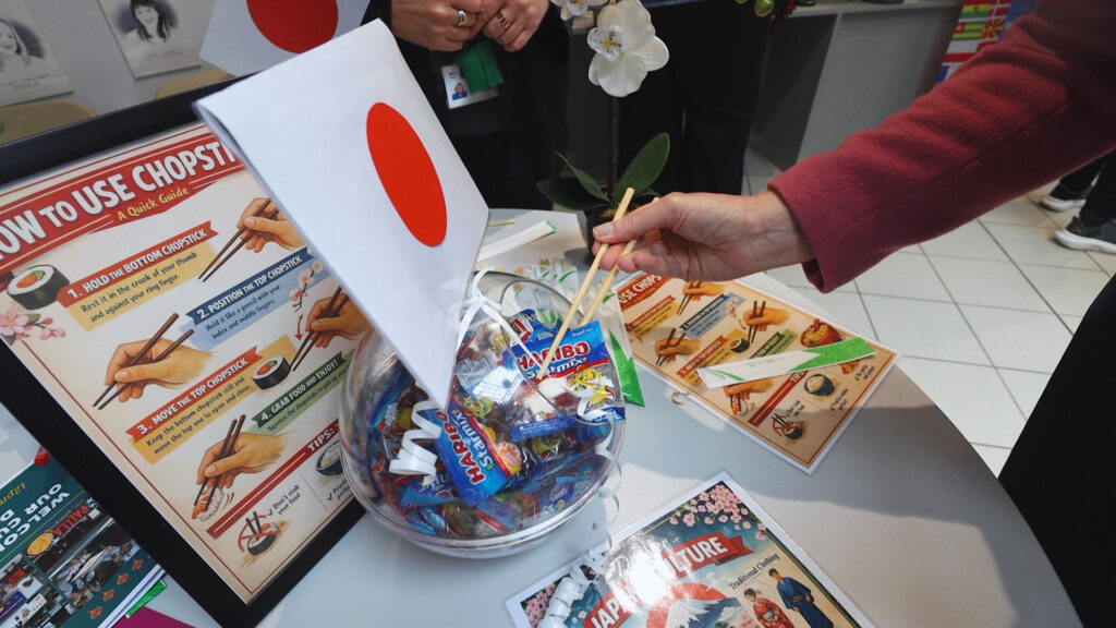 On a table there is a fishbowl filled with sweets and a Japanese flag. Someone is using chopsticks to grab the sweets