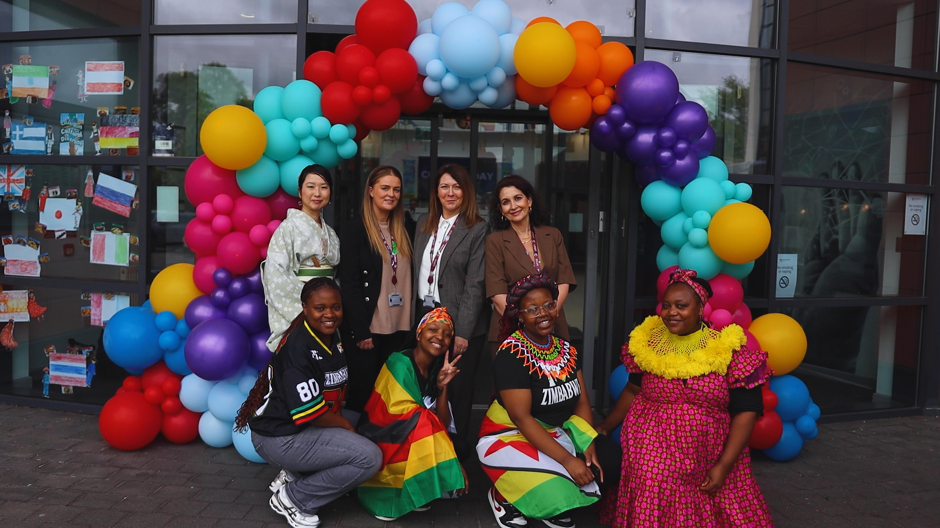 a group of people are smiling for a photo, standing outside a balloon arch