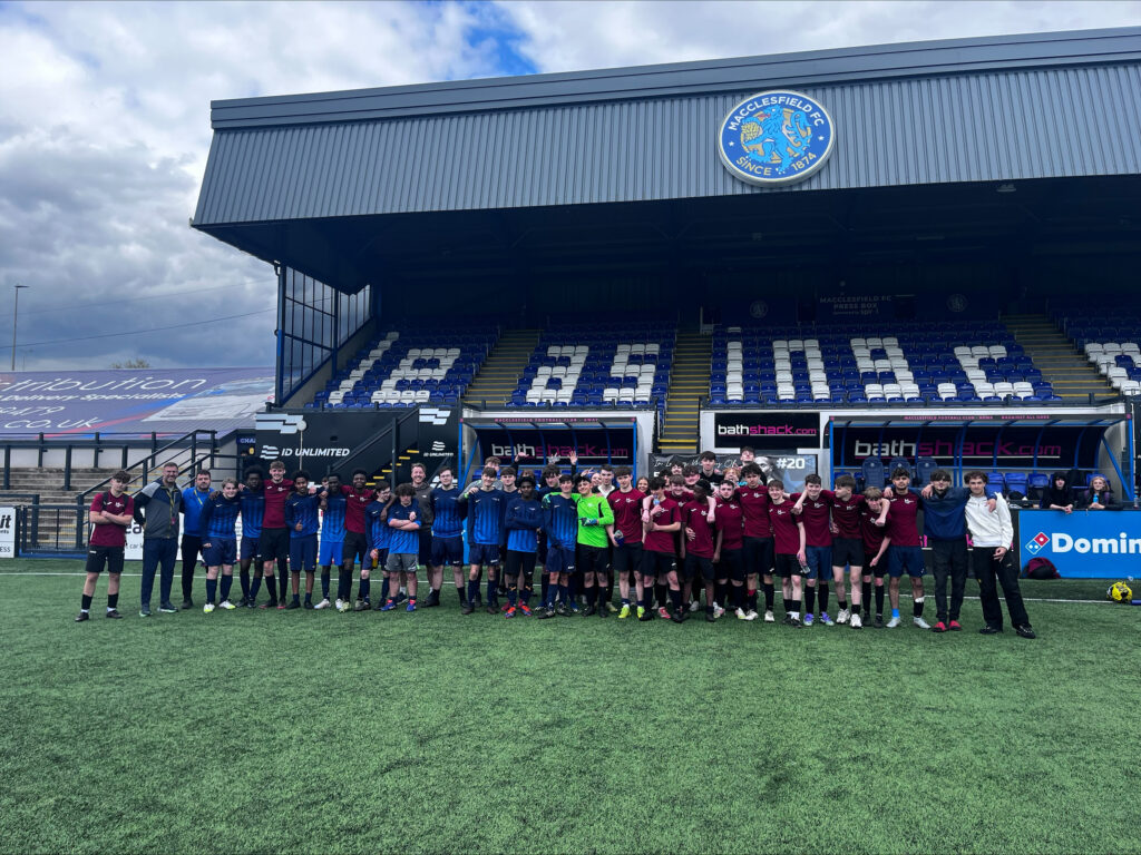 a group of students wearing football kits are standing on a football pitch smiling for a photo