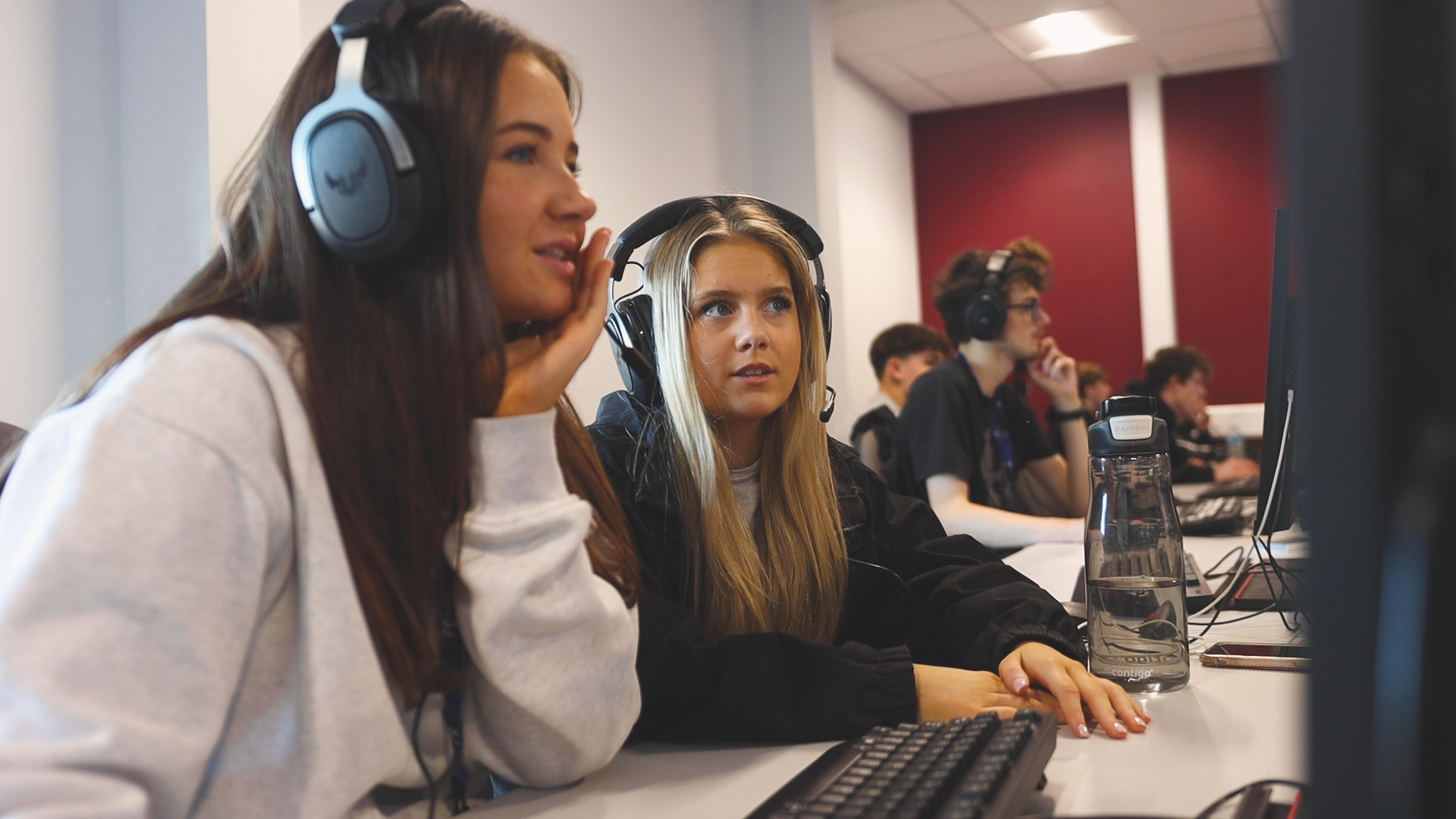two students are wearing headphones whilst working on computers
