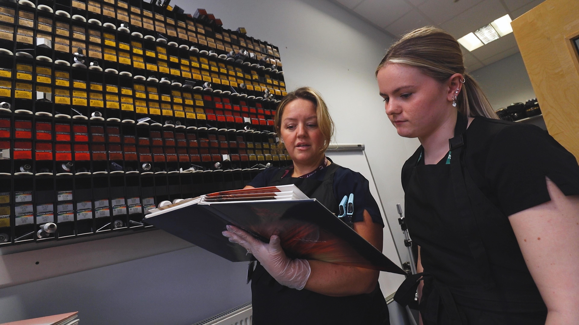 a hairdressing teacher and student look at documents on a clipboard