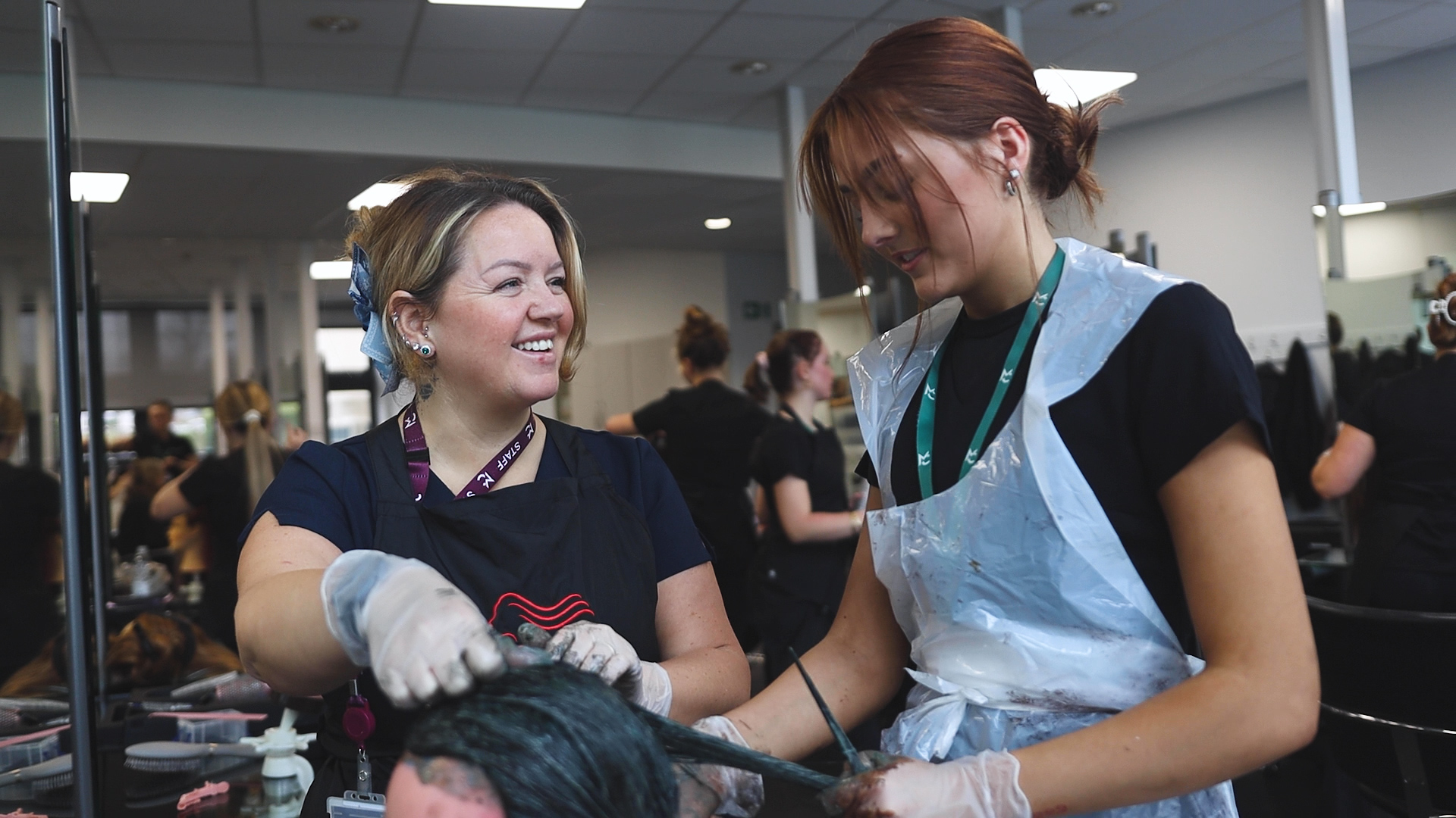 a hairdressing teacher watches as a student colours a client's hair