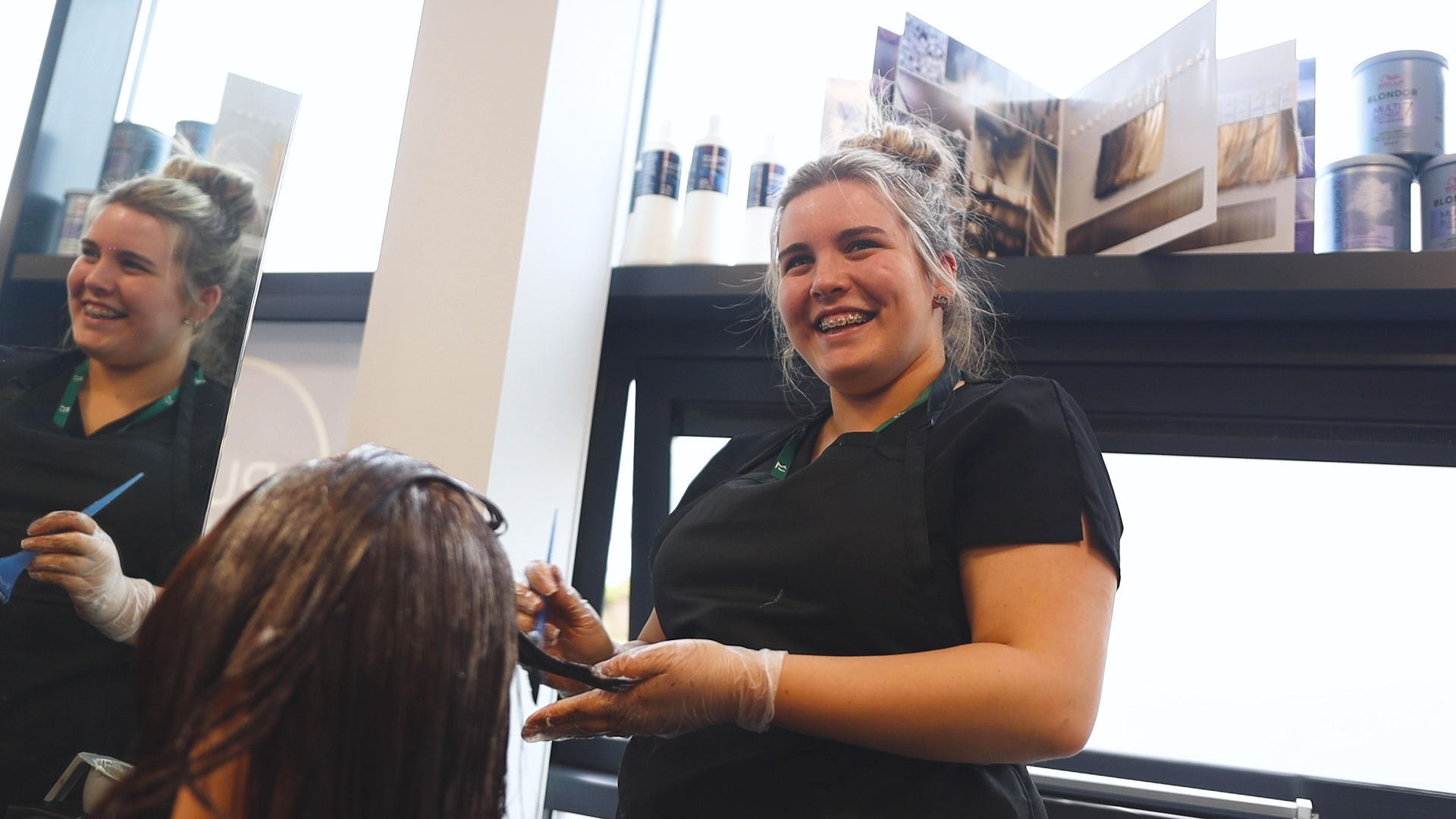 a hairdressing student smiles as they practice hair colouring techniques
