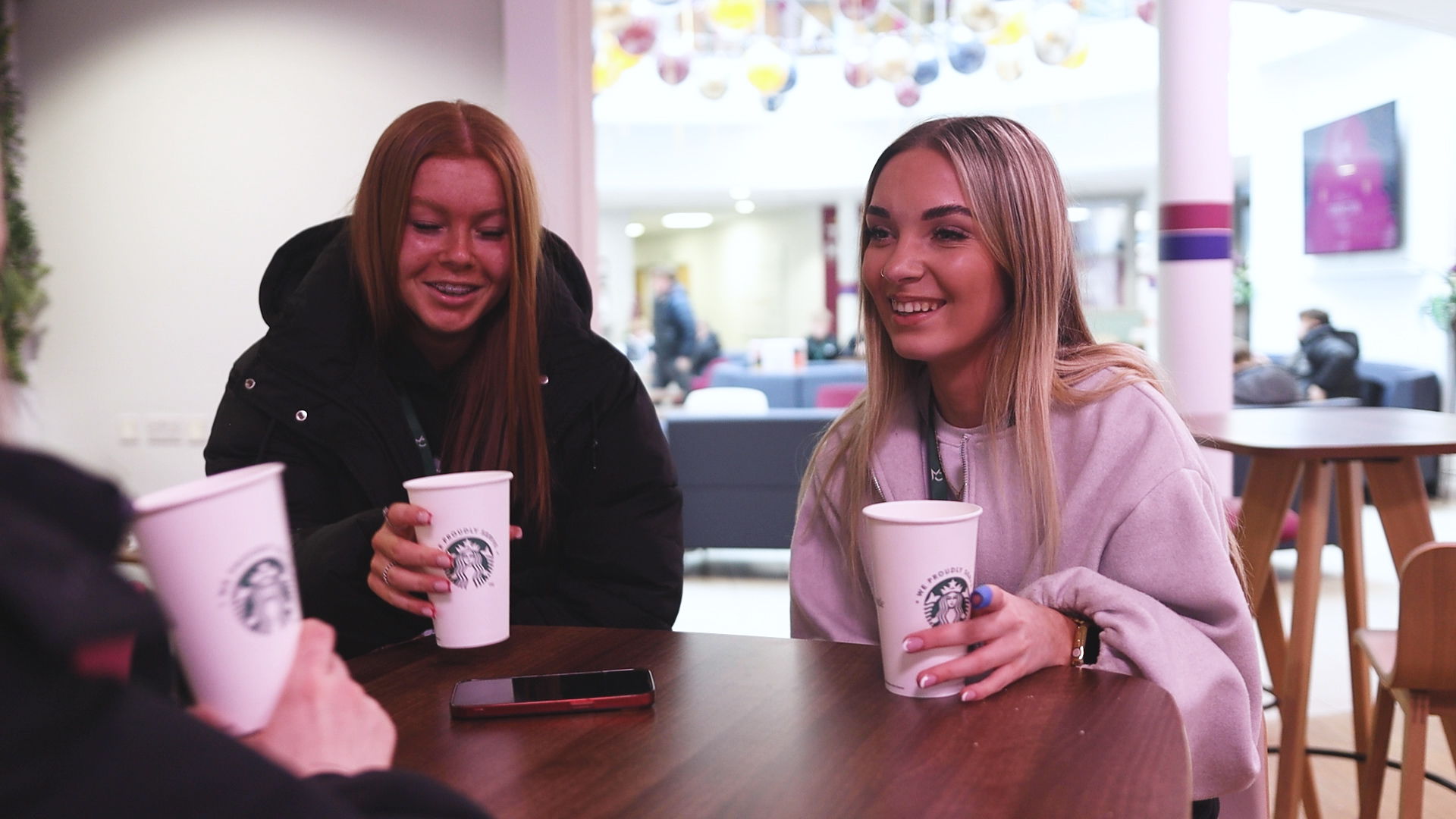 two students with coffee cups sitting in a cafe