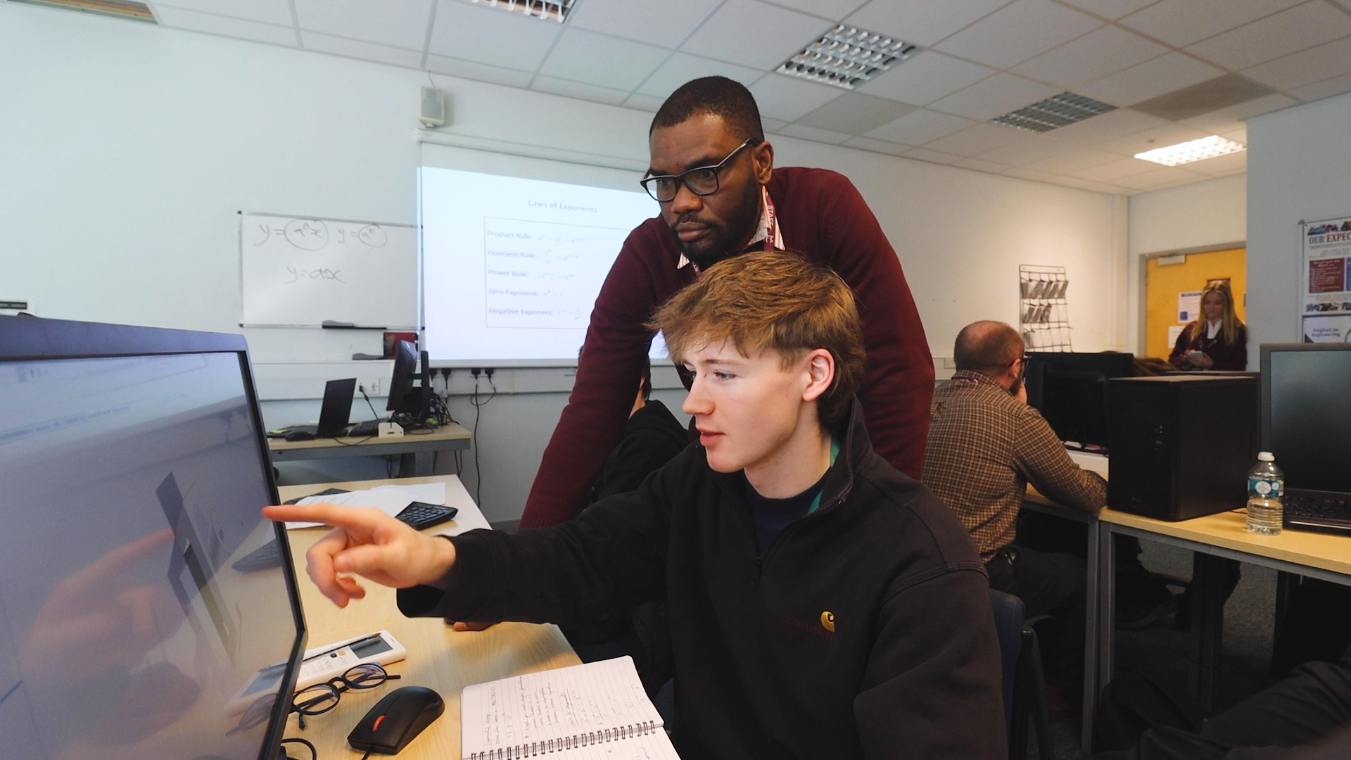 An engineering student and teacher are looking at computer. On the computer, there is an engineering design done by CAD