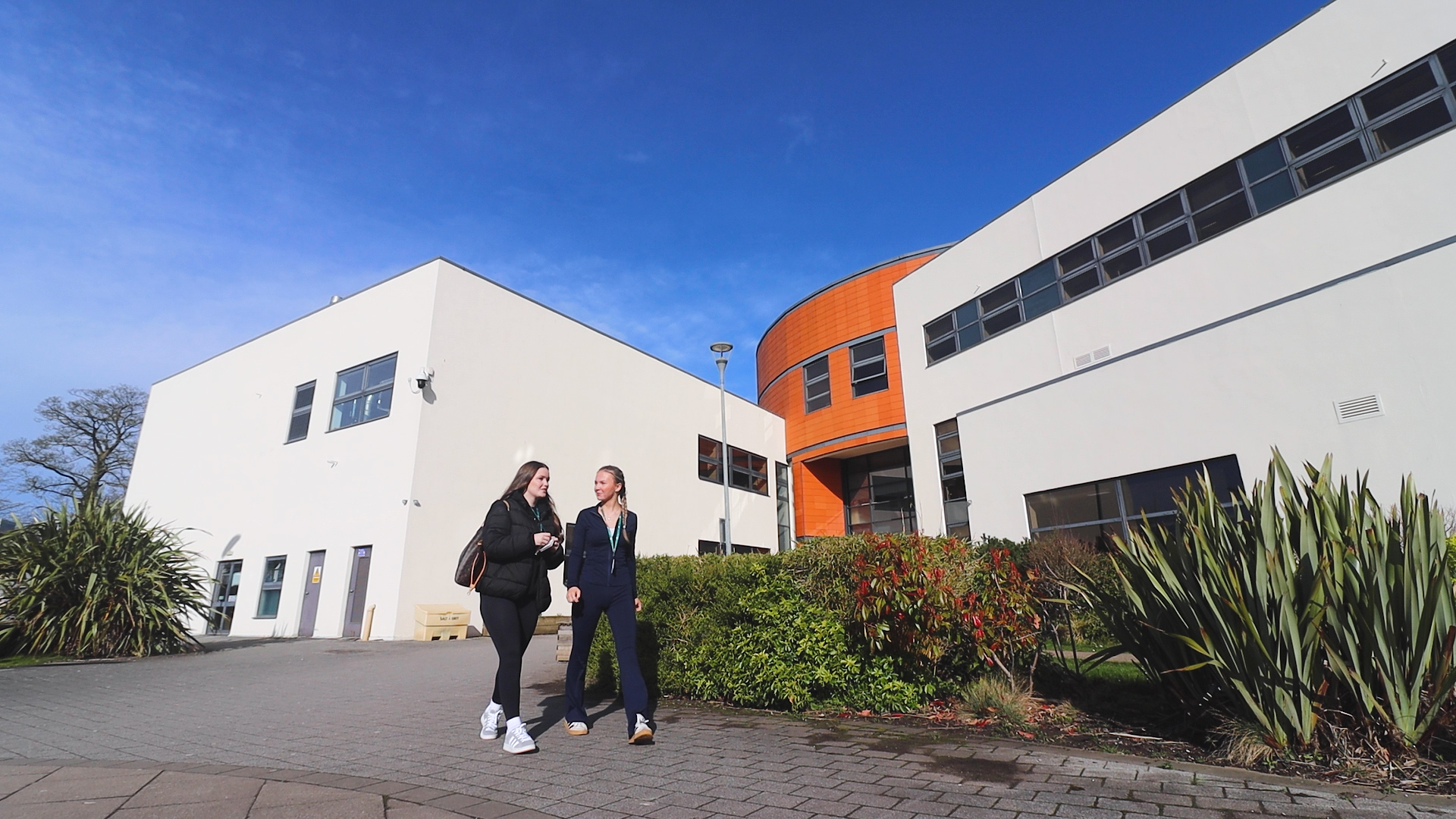 two students walking by the college smiling