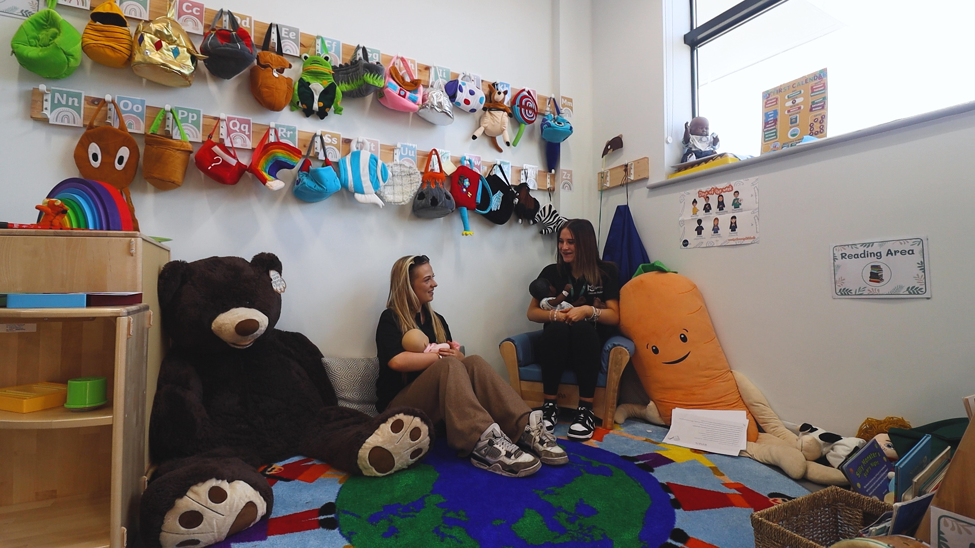 Two childcare students are sitting in the Childcare Skills Hub holding plastic babies