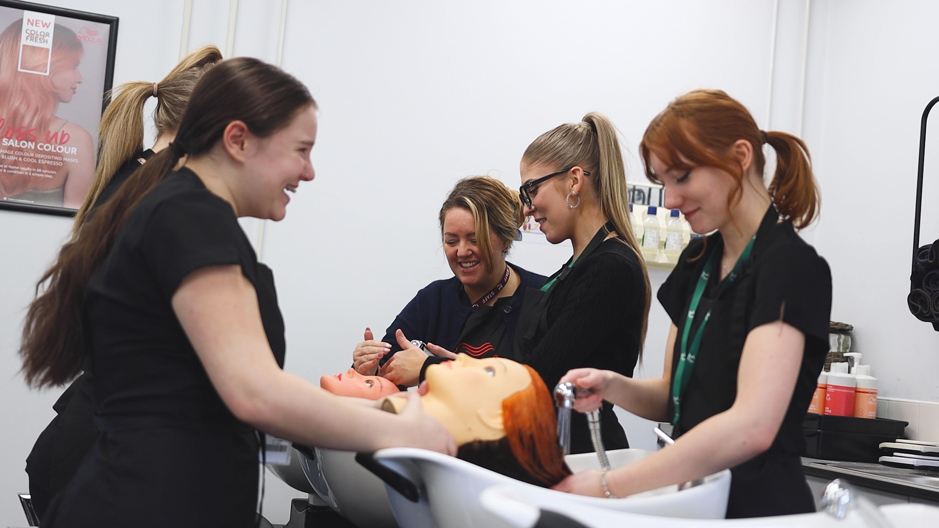 hairdressing students practice washing hair techniques on a mannequin head while a teacher watches