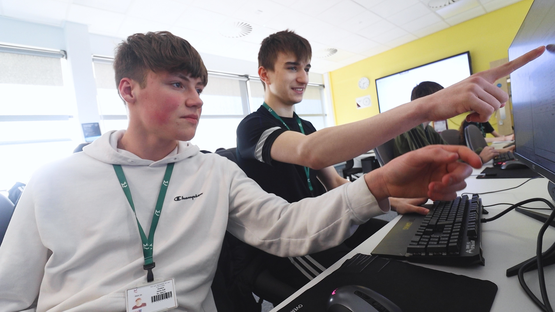 two students are sitting at a desk, pointing at a computer
