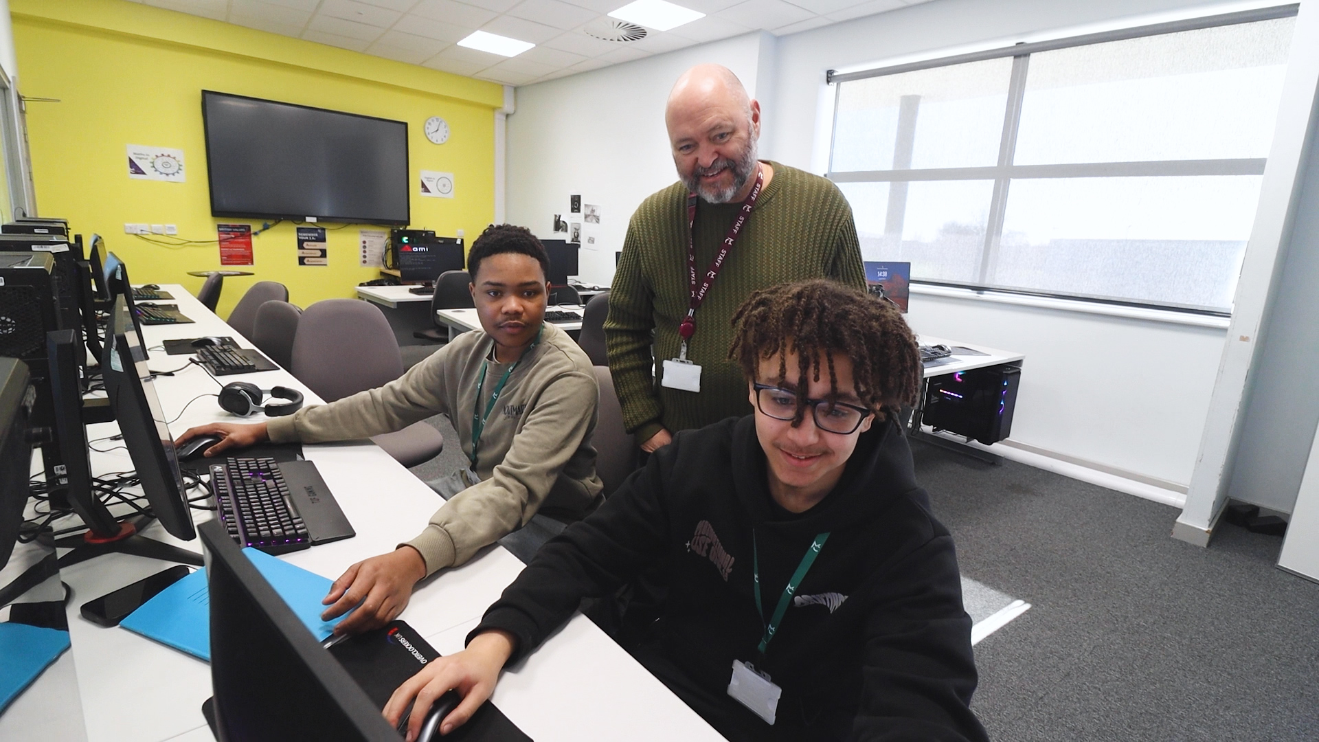 Two students work on computers while an IT watches them