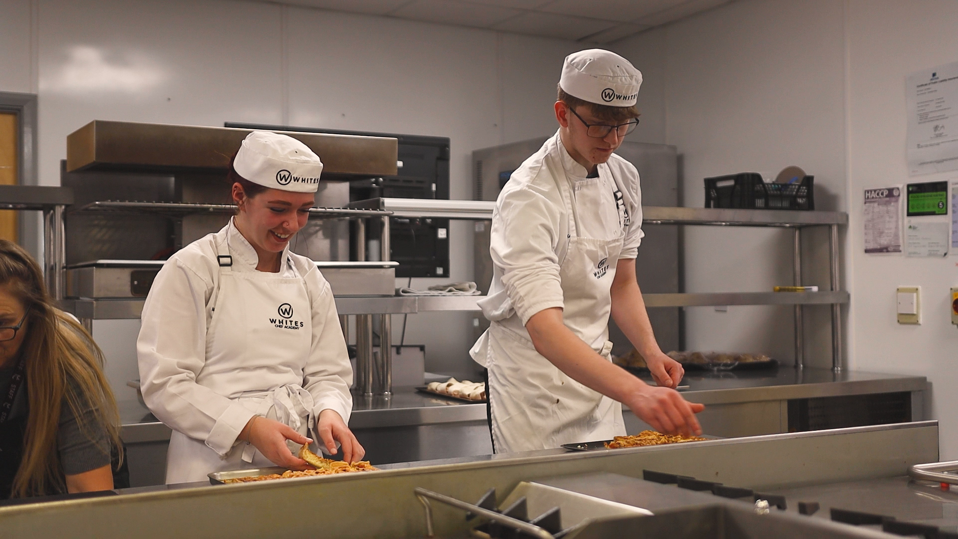 two students dressed in chef uniforms working in a kitchen