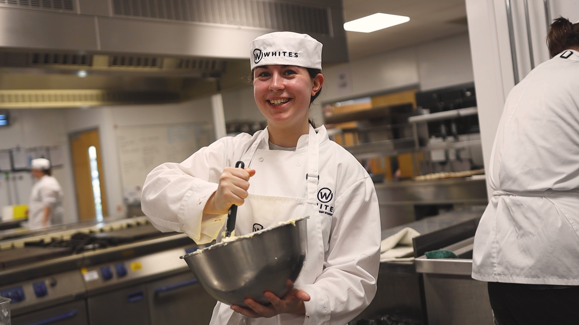a student wearing a chef uniform is mixing a bowl